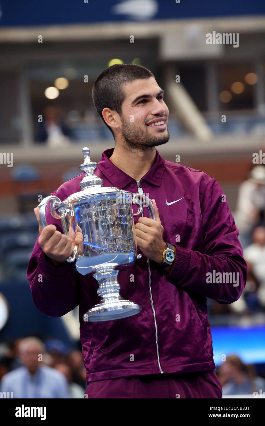 7 settembre 2025 - Flushing Meadows, New York - il secondo posto di testa di serie Carlos Alcaraz dello spagnolo detiene il trofeo US Open dopo aver sconfitto Jannik Sinner dell'Italia, in background, nella finale maschile. Foto Stock