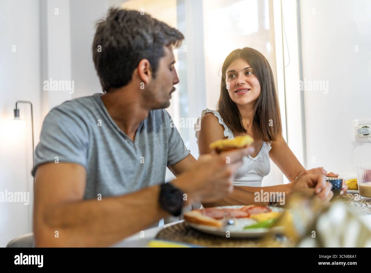 Giovani coppie che condividono un pasto e una conversazione al loro tavolo in cucina, godendosi una mattinata rilassante insieme Foto Stock
