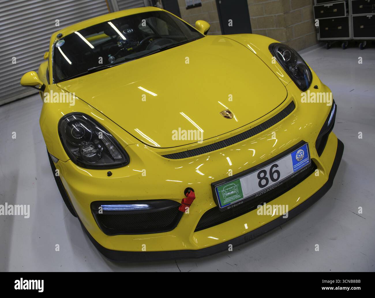 Foto dinamica davanti a un'auto sportiva Porsche Cayman GT4 gialla con cinghia di traino rossa montata sulla parte anteriore sinistra, internazionale Foto Stock