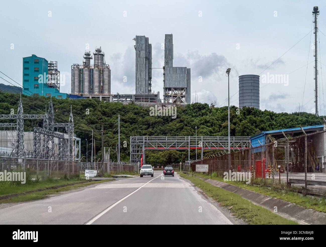 Batangas (Simlong), Filippine. 20 settembre 2025. Il complesso petrolchimico del JG Summit, il più grande produttore e operatore di poliolefine delle Filippine dell'unico cracker a vapore del paese, si affaccia sulla strada costiera attraversata da ponti di cremagliere con condutture industriali. Unità di cracking e polimeri di nafta, colonne di distillazione, silos in acciaio inox e edificio di processo sorgono dietro la collina. L'espansione del sito è stata inaugurata nel 2024 da Pres. Marcos. L: Sottostazione elettrica alimenta la zona industriale. R: Grande silo cilindrico grigio del terminale CEMEX/APO per cemento. Crediti: Kevin Izorce/Alamy Live News Foto Stock