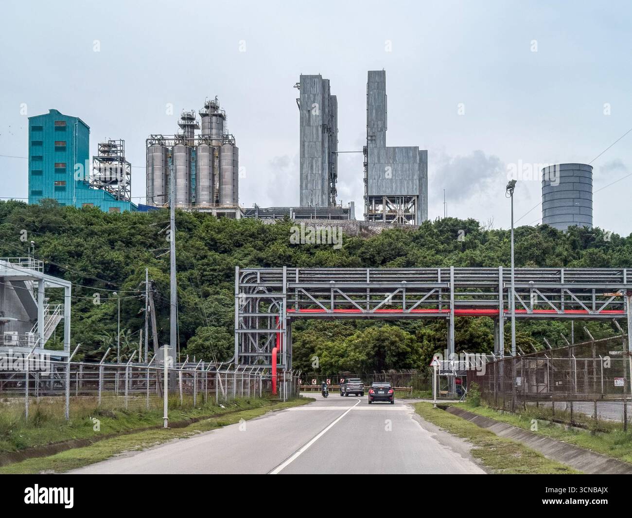 Batangas (Simlong), Filippine. 20 settembre 2025. Il complesso petrolchimico del JG Summit, il più grande produttore e operatore di poliolefine delle Filippine dell'unico cracker a vapore del paese, si affaccia sulla strada costiera attraversata da ponti di cremagliere con condutture industriali. Unità di cracking e polimeri di nafta, colonne di distillazione, silos in acciaio inox e edificio di processo sorgono dietro la collina. L'espansione del sito è stata inaugurata nel 2024 da Pres. Marcos. L: Sottostazione elettrica alimenta la zona industriale. R: Grande silo cilindrico grigio del terminale CEMEX/APO per cemento. Crediti: Kevin Izorce/Alamy Live News Foto Stock