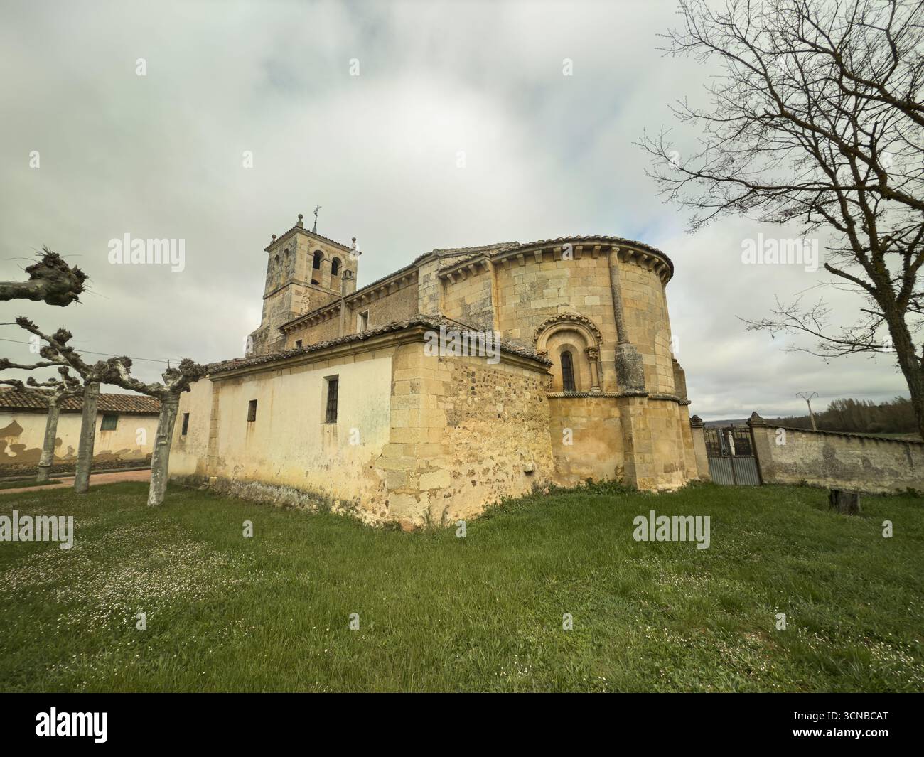 Storica chiesa romanica con abside e torre, circondata da erba e alberi Foto Stock