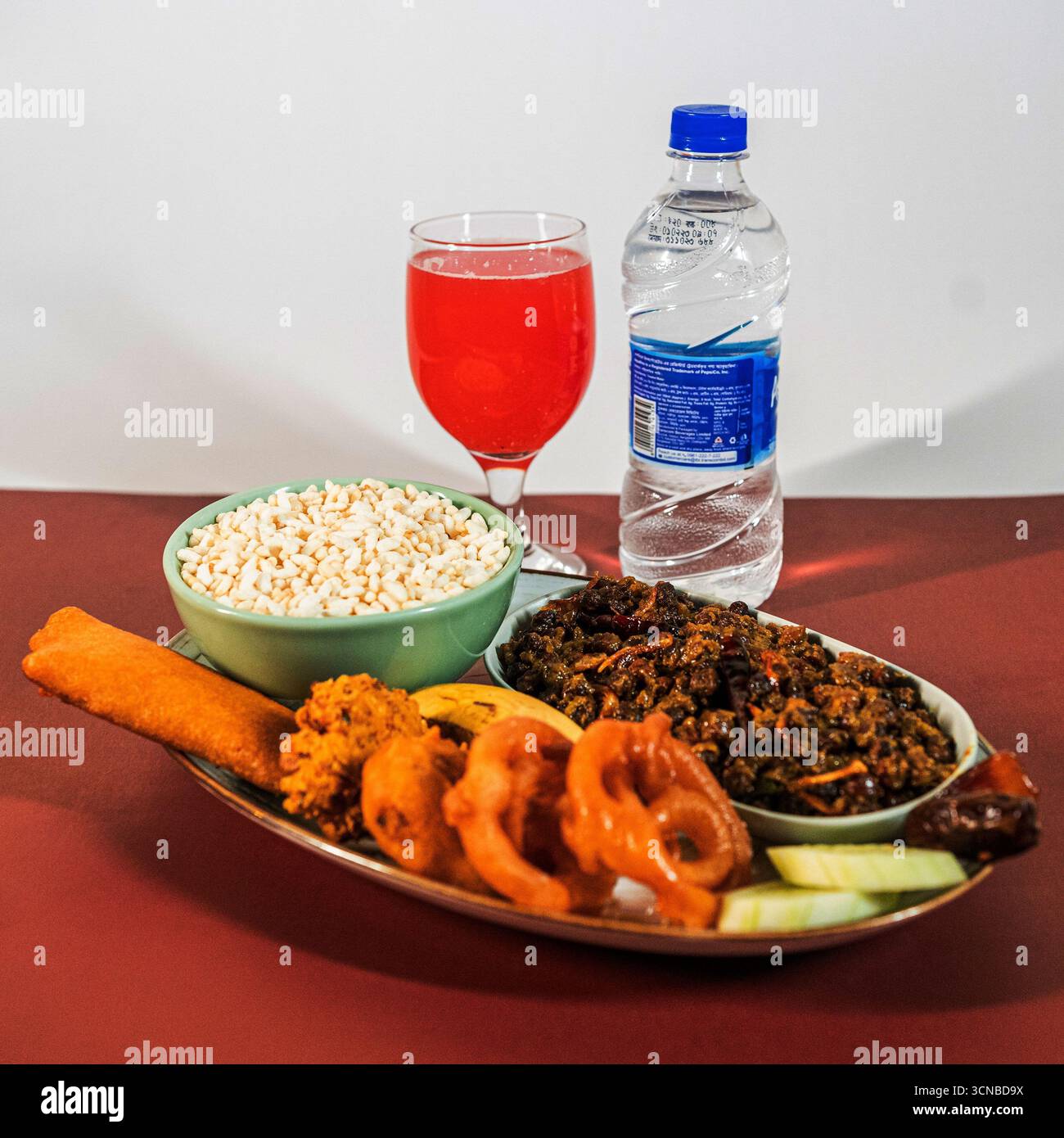 Un piatto tradizionale Iftar con una ciotola di riso soffiato, spuntini salati fritti, un piatto di carne o lenticchie, un bicchiere di succo e una bottiglia d'acqua. Foto Stock