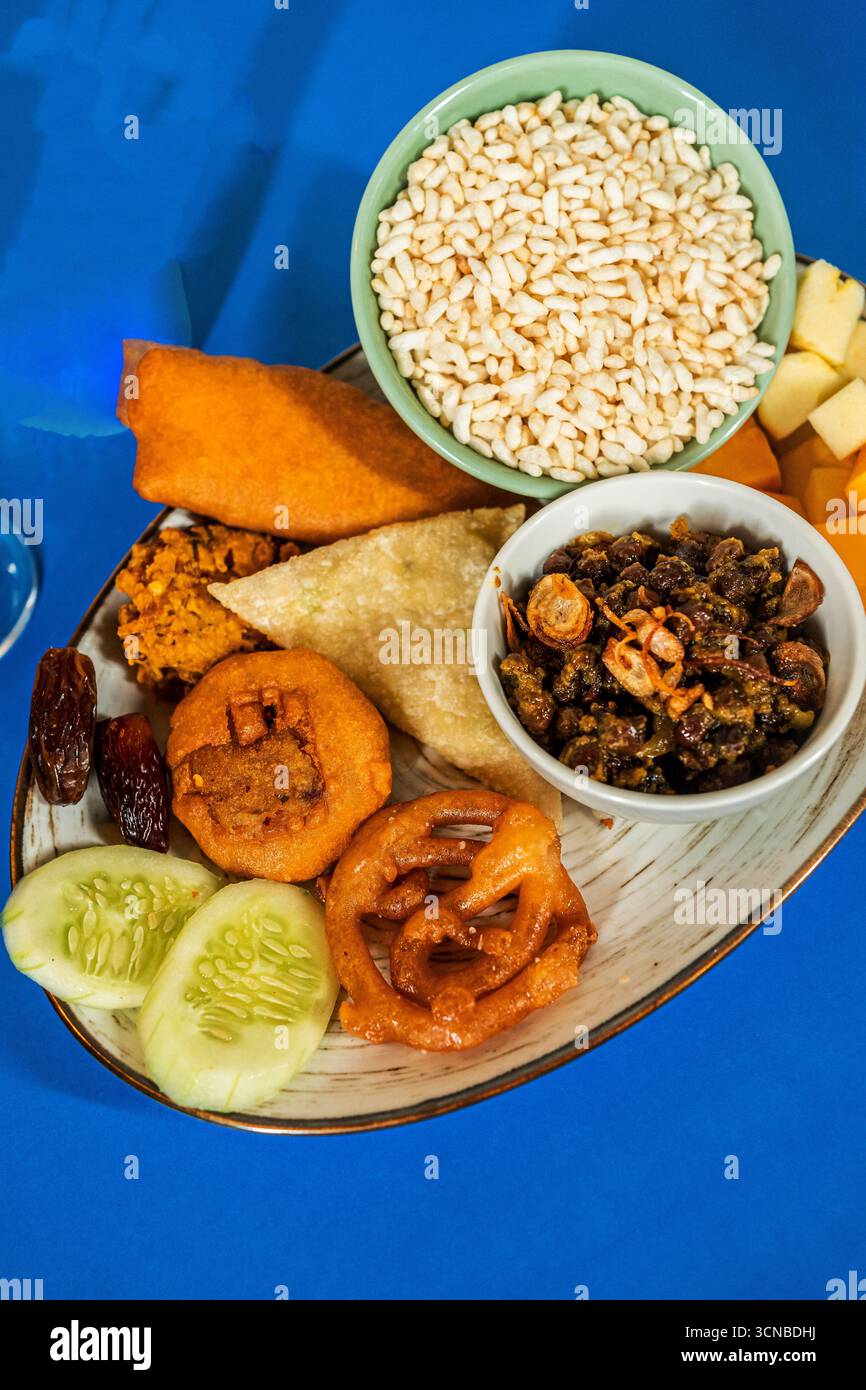 Uno scatto dall'alto di un tradizionale piatto di Iftar dell'Asia meridionale su sfondo blu. Il piatto include piatti dolci e salati, una bevanda e una bottiglia Foto Stock