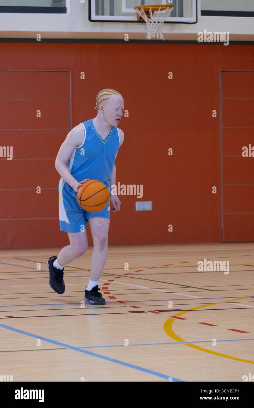 Pallacanestro arancione che rimbalza sul campo da palestra in legno contrassegnato da linee colorate sotto la parete imbottita Foto Stock