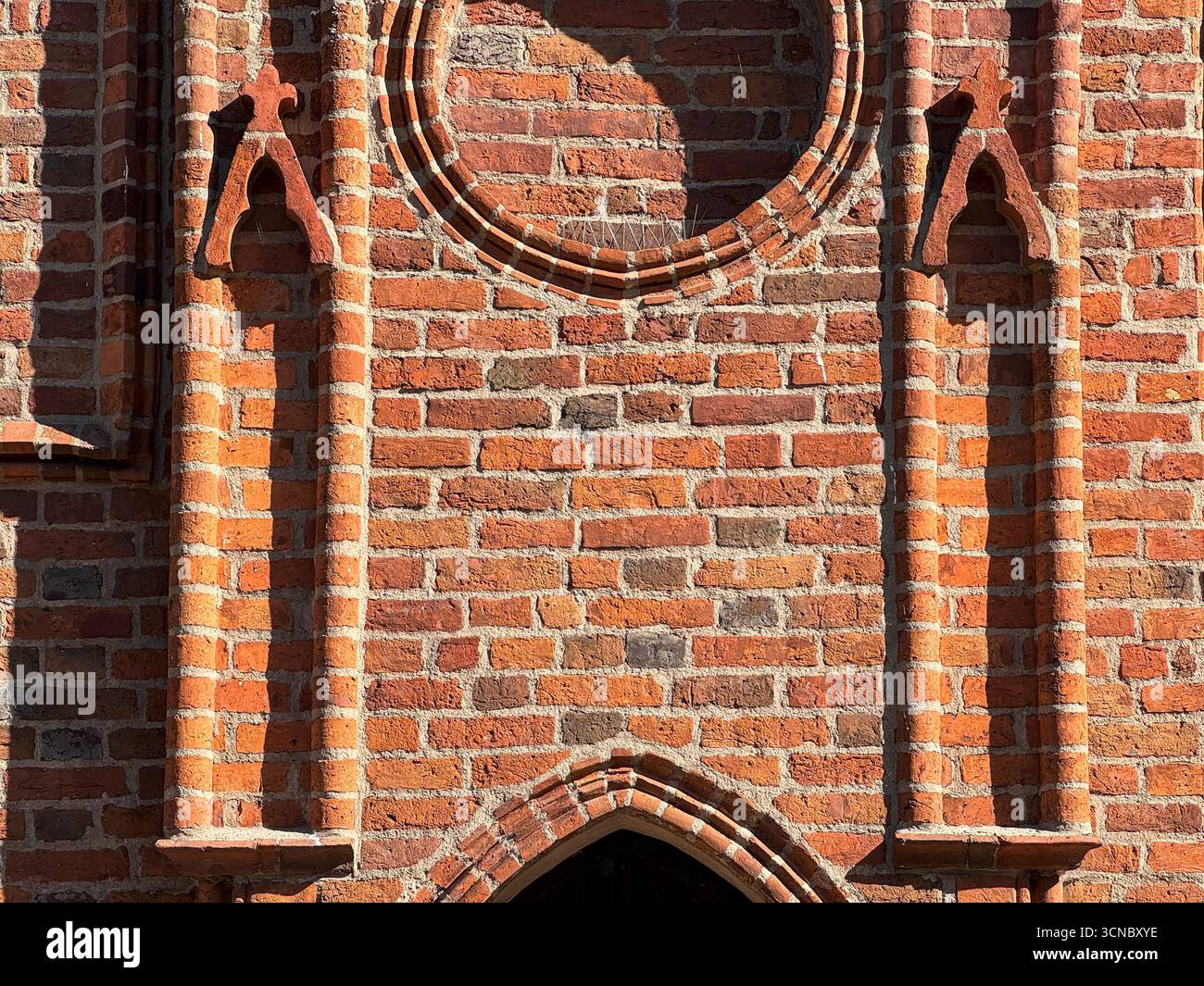 Vista dettagliata della facciata gotica della chiesa costruita nel 1370 in Europa che mostra ornamenti circolari in mattoni e ingresso ad arco a punta. Architettura cattolica medievale Foto Stock