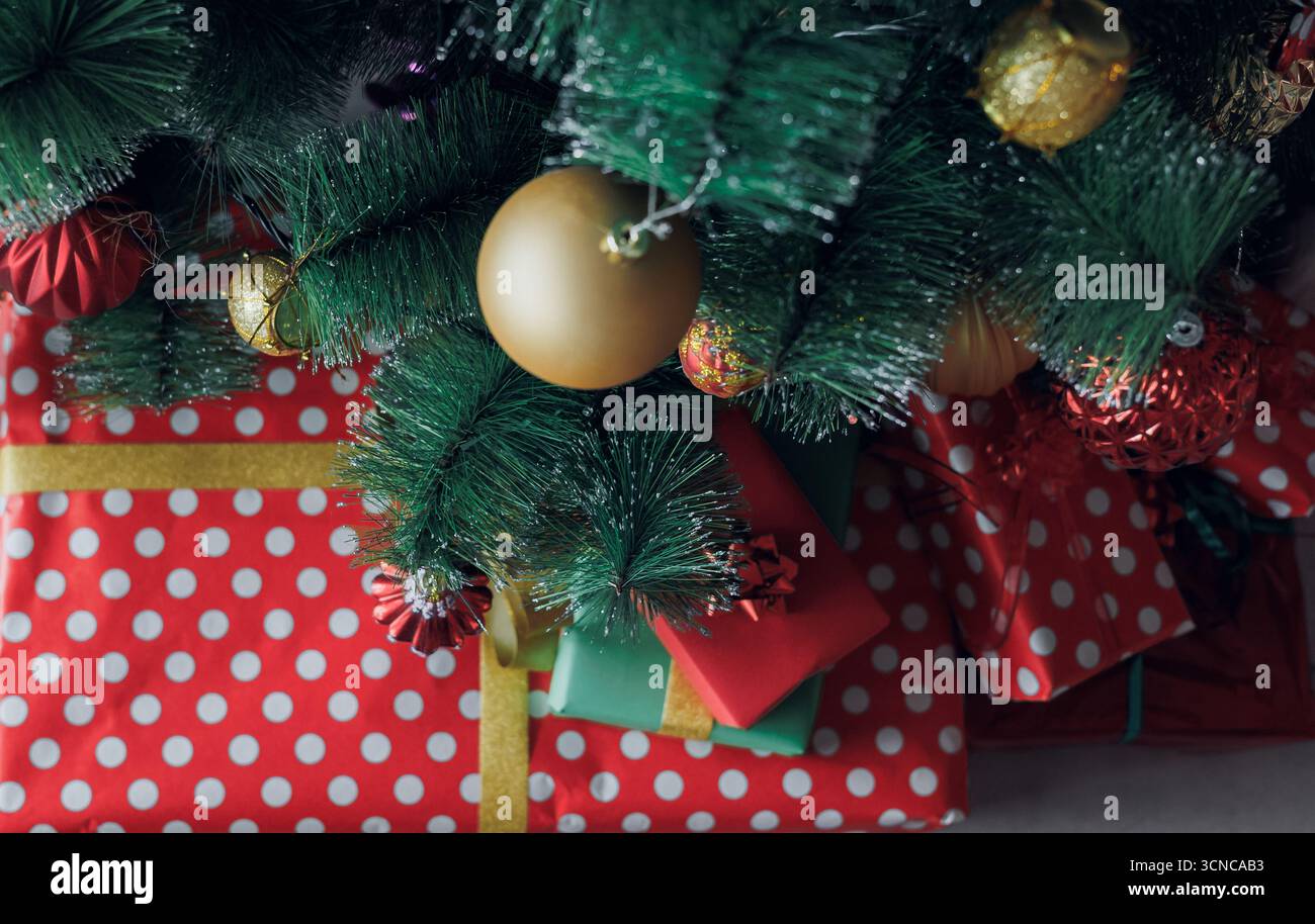 Primo piano di regali e ornamenti natalizi sotto un albero decorato, mostrando colori, texture e atmosfera natalizia per i disegni stagionali Foto Stock