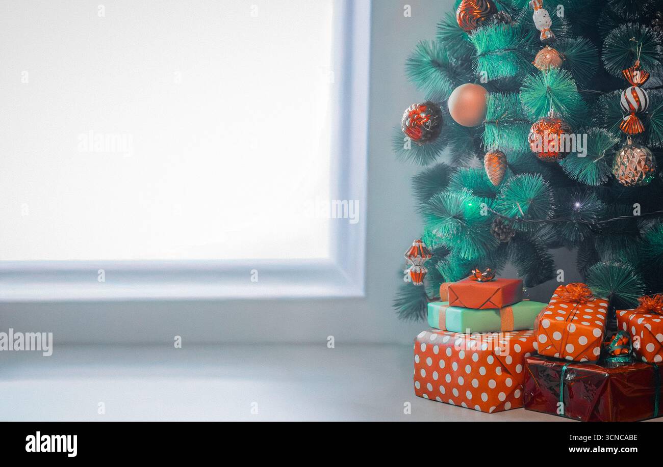 Regali natalizi e un albero di Natale accanto a una grande finestra Foto Stock