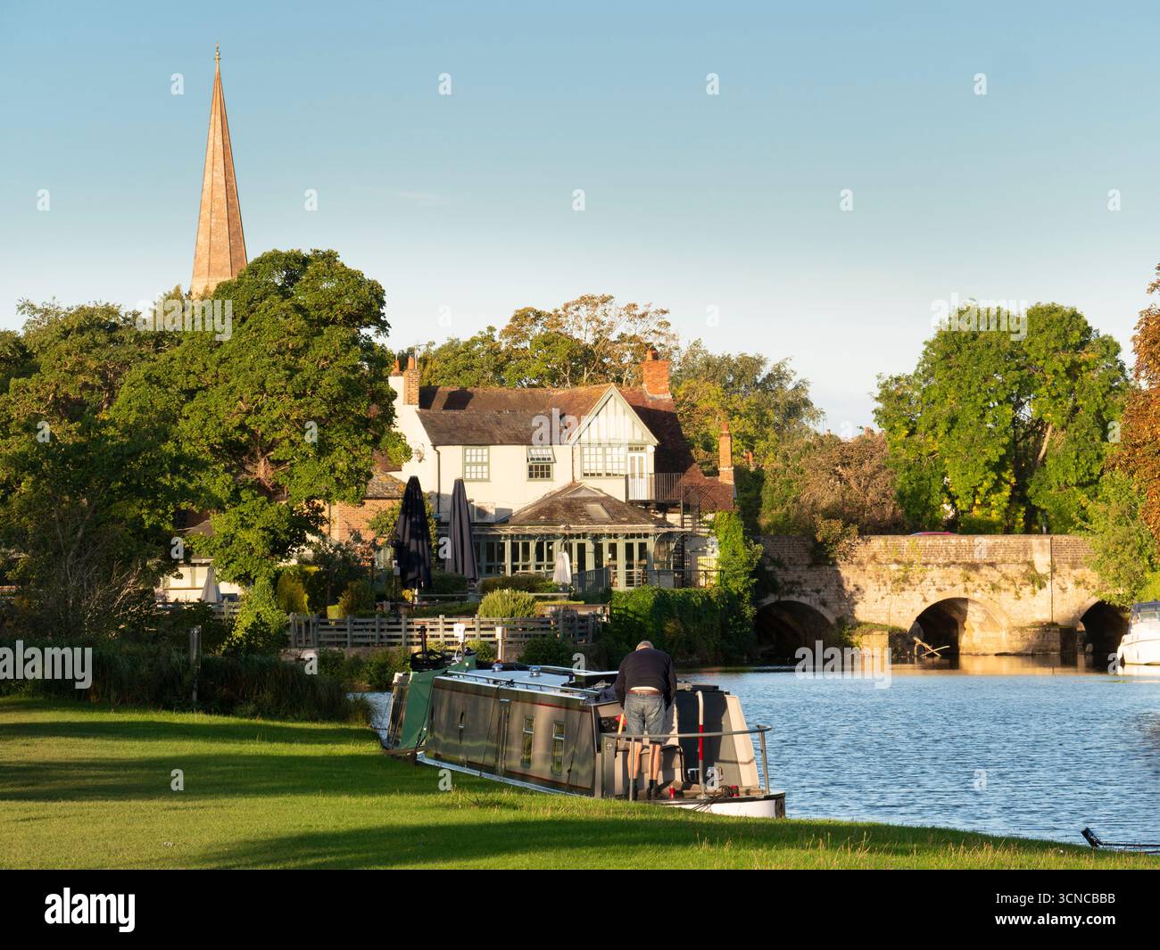 Casa galleggiante ormeggiata sul Tamigi ad Abingdon. Una bella vista del Tamigi ad Abingdon, in tarda mattinata d'estate. Siamo sulla riva sud del fiume, guardando da un'altra parte del ponte medievale di Abingdon. Ancora più antica è la guglia della chiesa anglosassone di Sant'Elena. Foto Stock