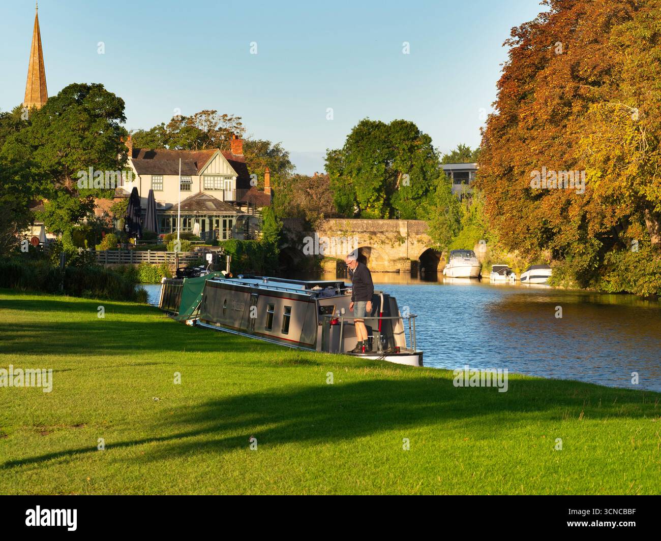 Casa galleggiante ormeggiata sul Tamigi ad Abingdon. Una bella vista del Tamigi ad Abingdon, in tarda mattinata d'estate. Siamo sulla riva sud del fiume, guardando da un'altra parte del ponte medievale di Abingdon. Ancora più antica è la guglia della chiesa anglosassone di Sant'Elena. Foto Stock