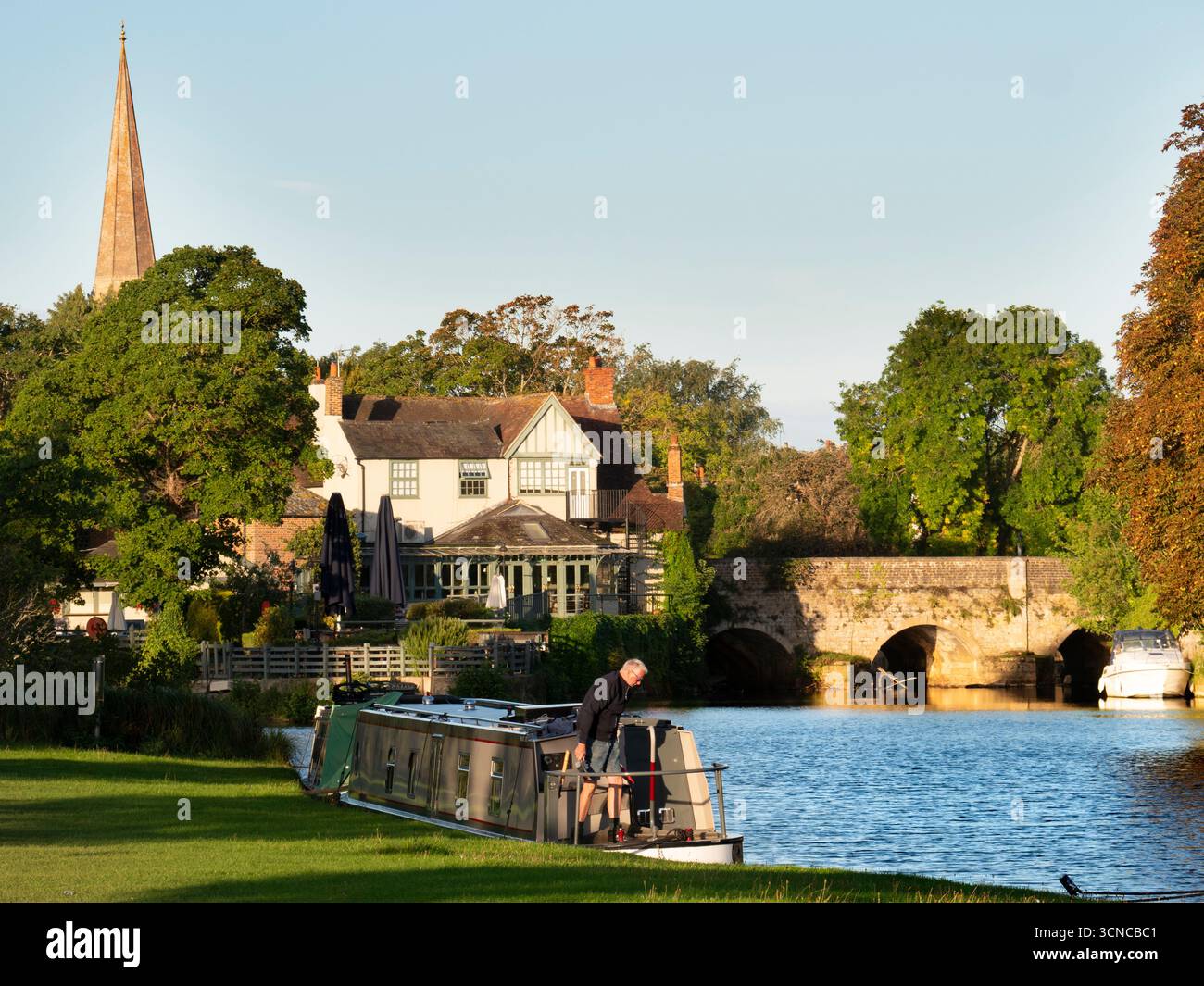Casa galleggiante ormeggiata sul Tamigi ad Abingdon. Una bella vista del Tamigi ad Abingdon, in tarda mattinata d'estate. Siamo sulla riva sud del fiume, guardando da un'altra parte del ponte medievale di Abingdon. Ancora più antica è la guglia della chiesa anglosassone di Sant'Elena. Foto Stock