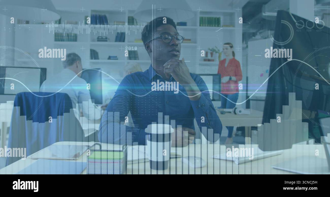 Analista dei dati che indossa una camicia blu che esamina i grafici del desktop sui monitor in un ufficio open space Foto Stock