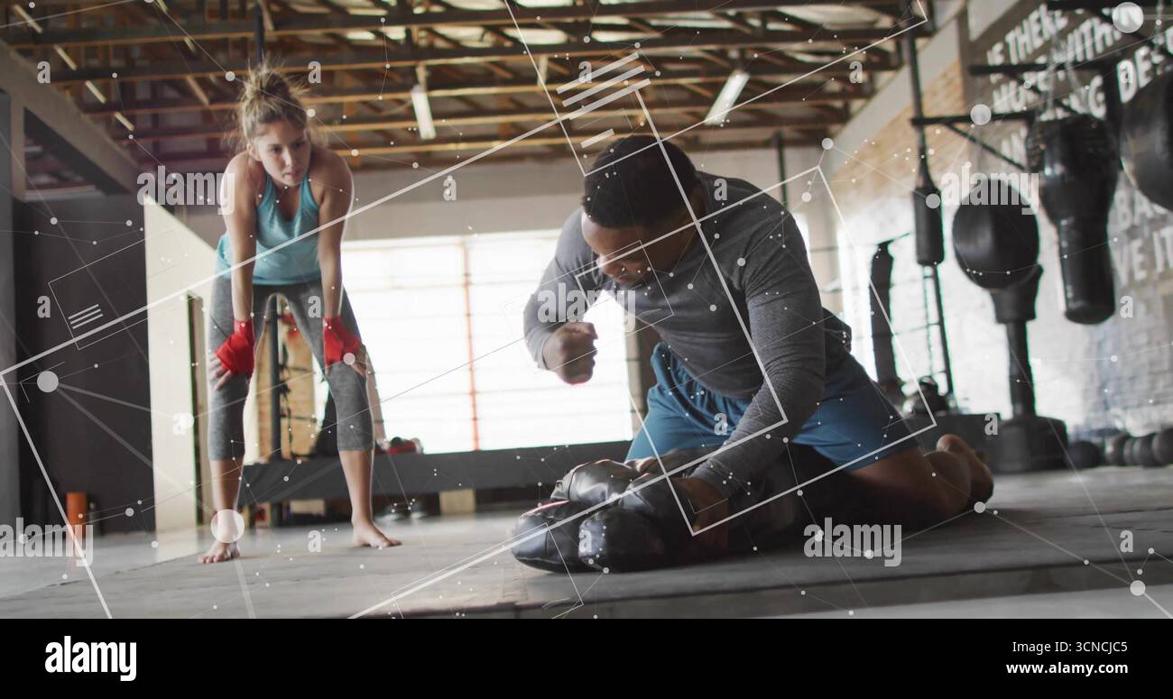 Pugni un afroamericano inginocchiato che fa strike nella palestra di pugilato, con guanti e borse pesanti Foto Stock