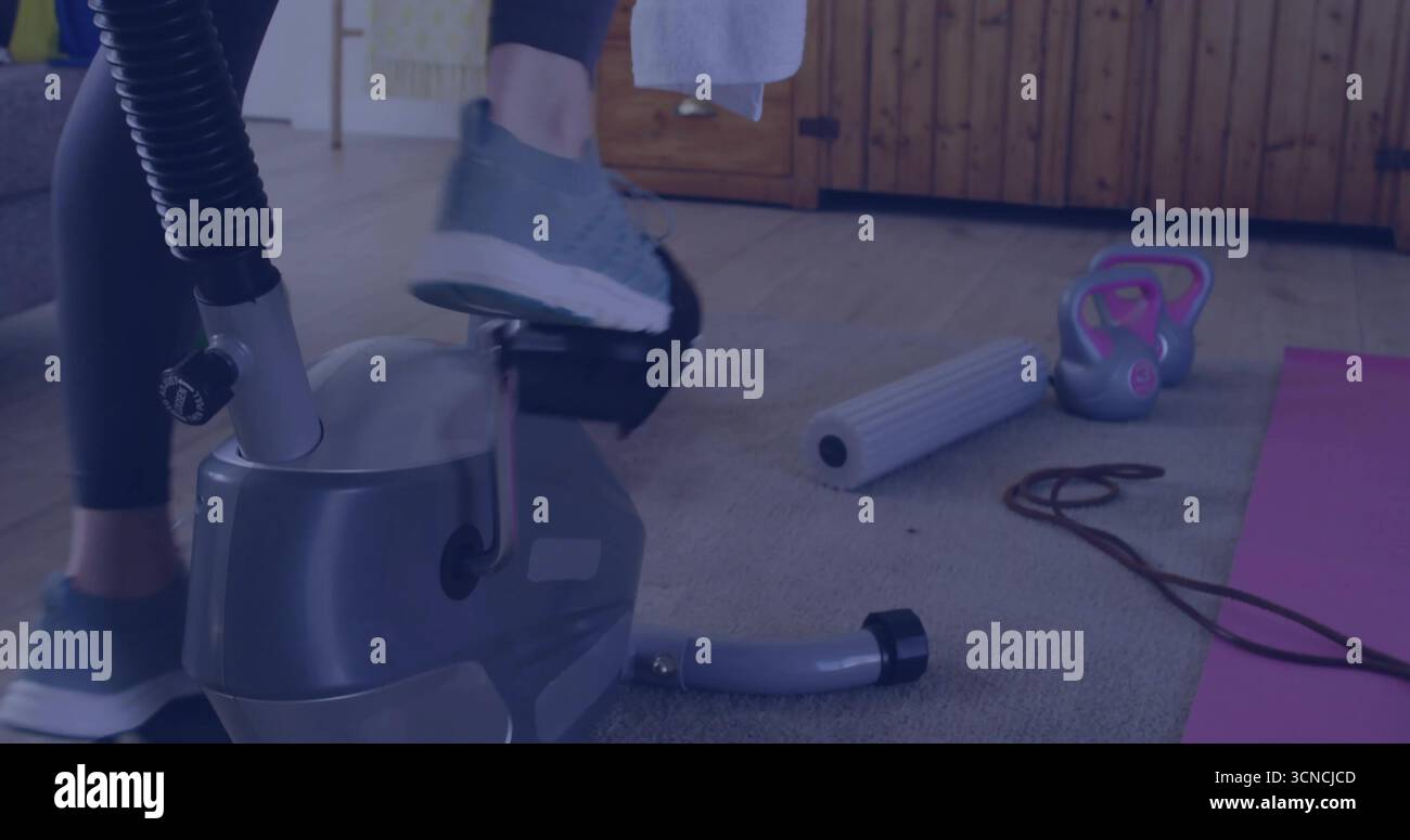 Pedalando donna in leggings scuri su cyclette in palestra, con rullo in schiuma e kettlebell Foto Stock