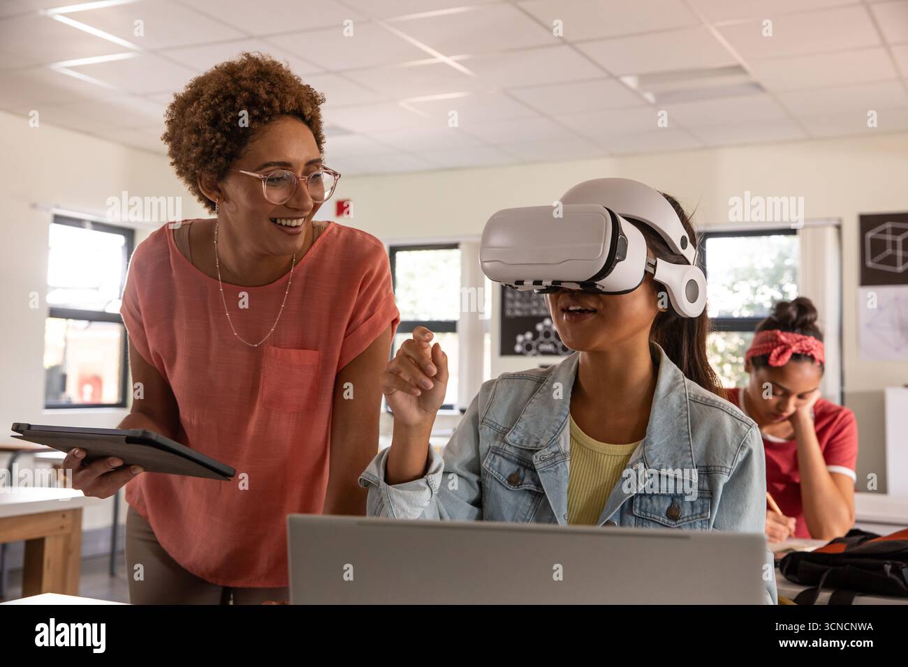 Insegnante afroamericano che guida gli studenti in realtà virtuale alla scrivania della classe con tablet e spazio di copia Foto Stock