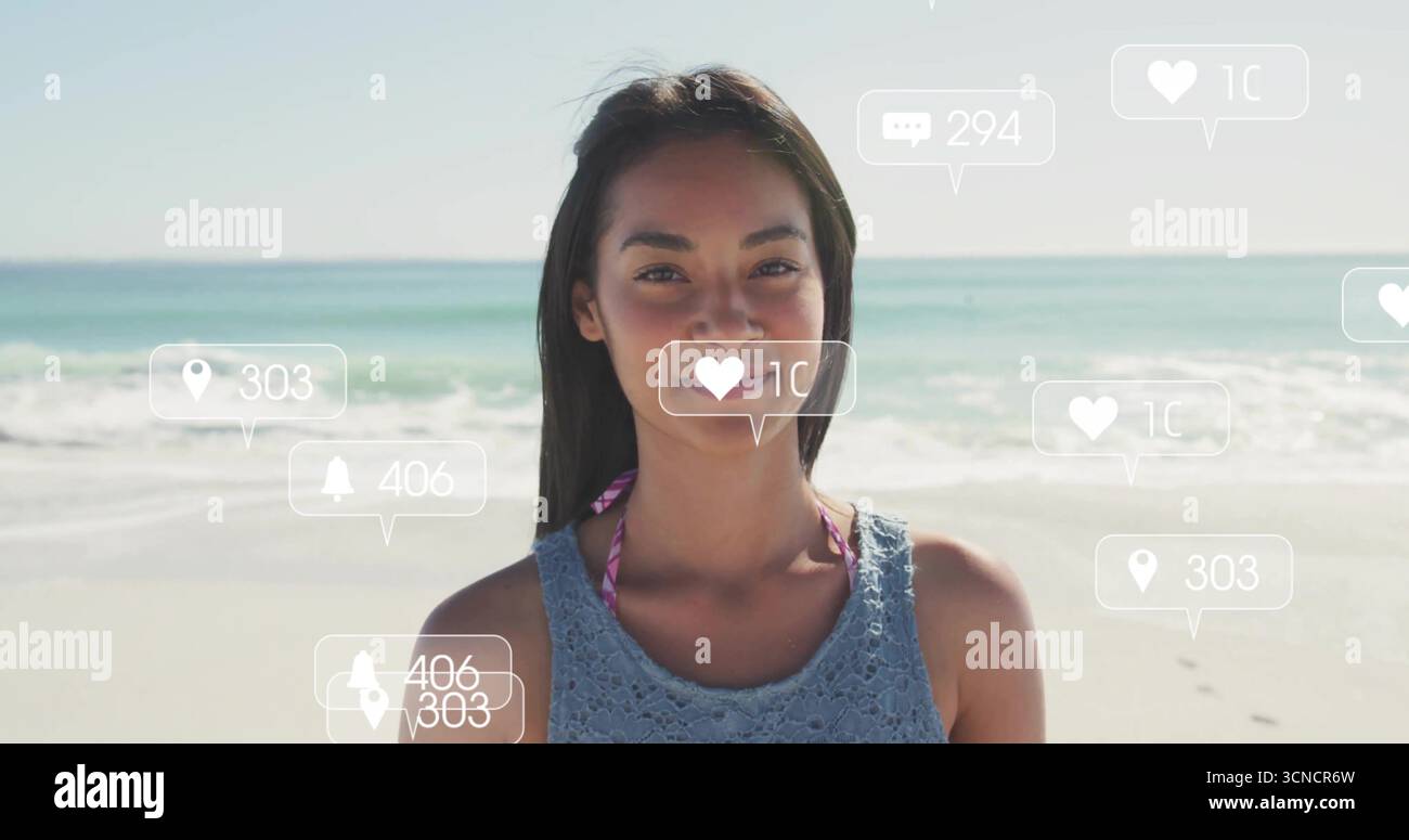 Donna in piedi che indossa il top a uncinetto blu sopra un bikini rosa sulla spiaggia, con icone fluttuanti dei social media Foto Stock