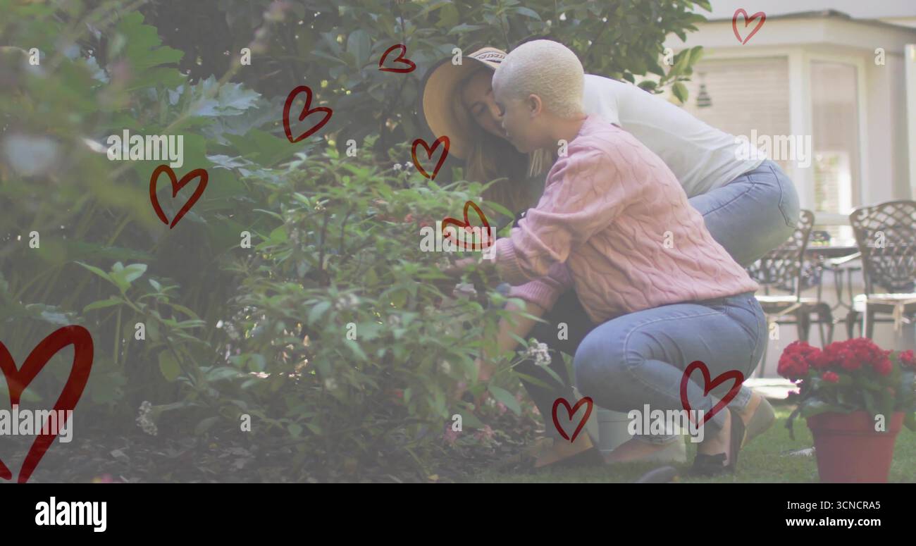 Coppia inginocchiato e potato arbusto nel giardino di fronte alla periferia, con fiori rossi e cappello di paglia Foto Stock