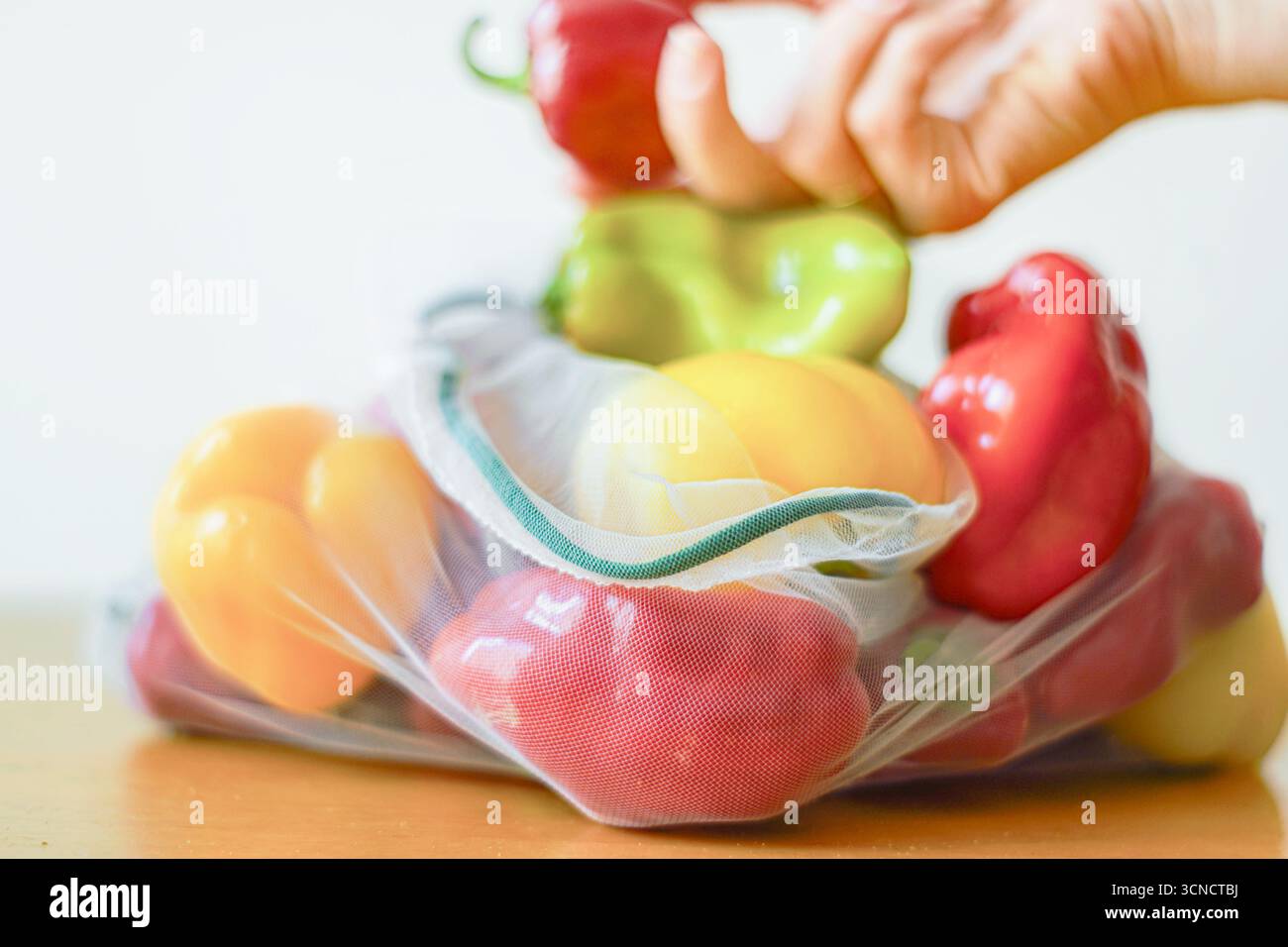 Peperoni multicolore in un sacchetto riutilizzabile ecologico e una mano che tiene in mano una paprika rossa sullo sfondo. Cultura da fattoria a tavola e dieta vegetariana Foto Stock