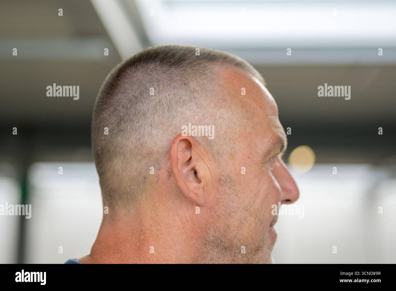 Profilo laterale ravvicinato di un uomo anziano con un taglio di capelli, in un ambiente interno moderno con luce naturale soffusa. Foto Stock