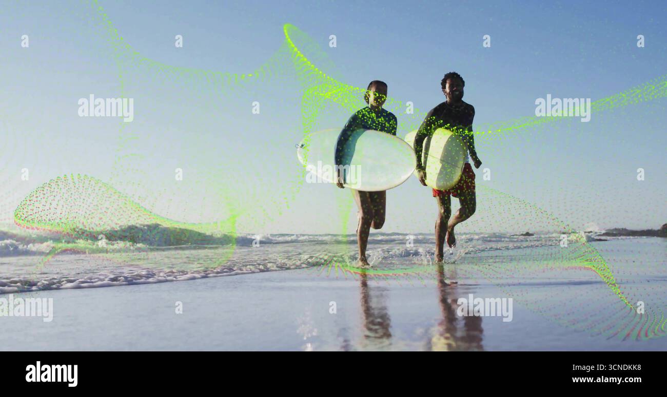 I surfisti che indossano le guardie di sicurezza che trasportano tavole da surf in spiaggia, con riflessi di sabbia bagnata Foto Stock