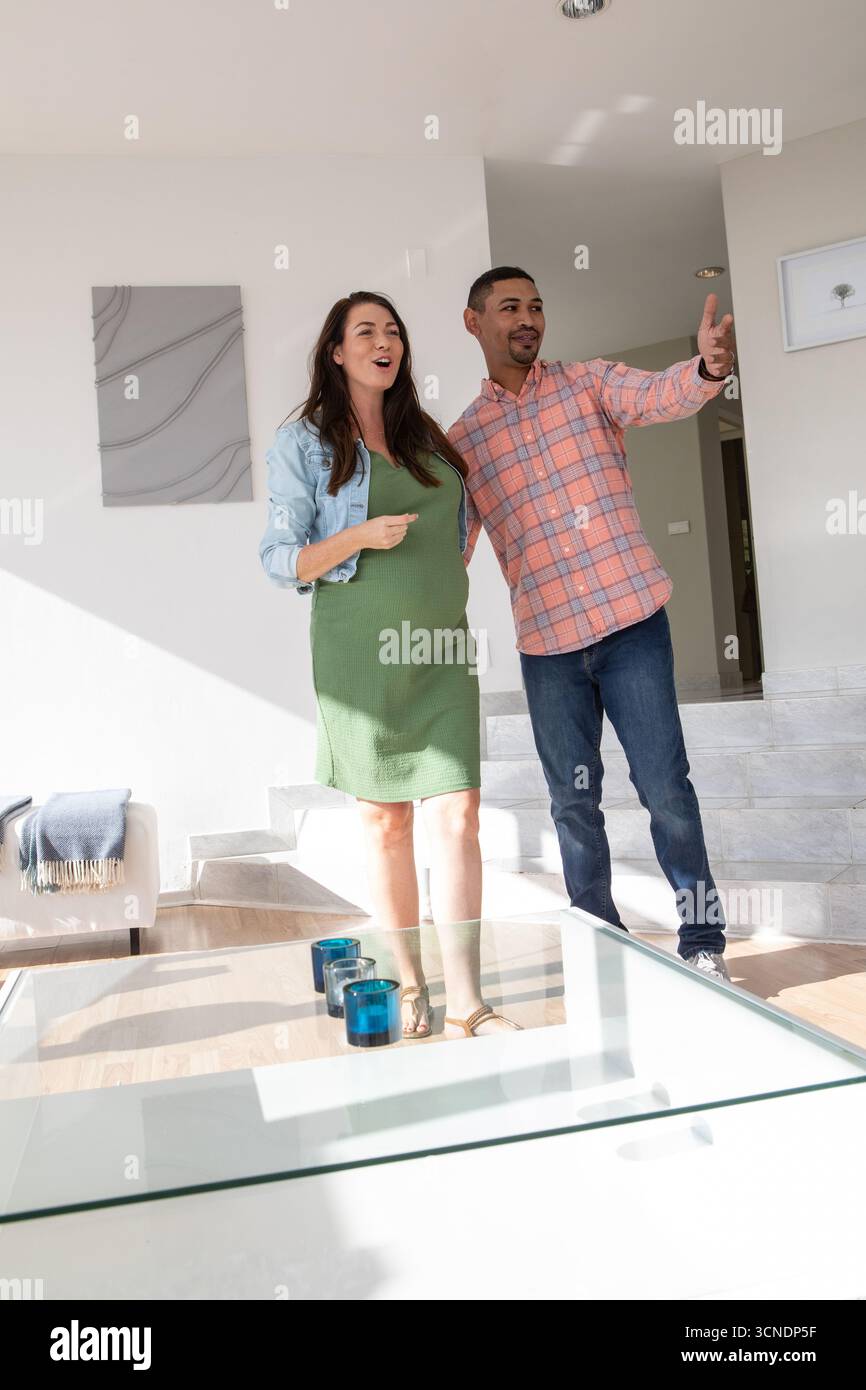 Coppia in piedi vicino al tavolino da caffè in vetro con portacandele blu che esplora il soggiorno contemporaneo Foto Stock