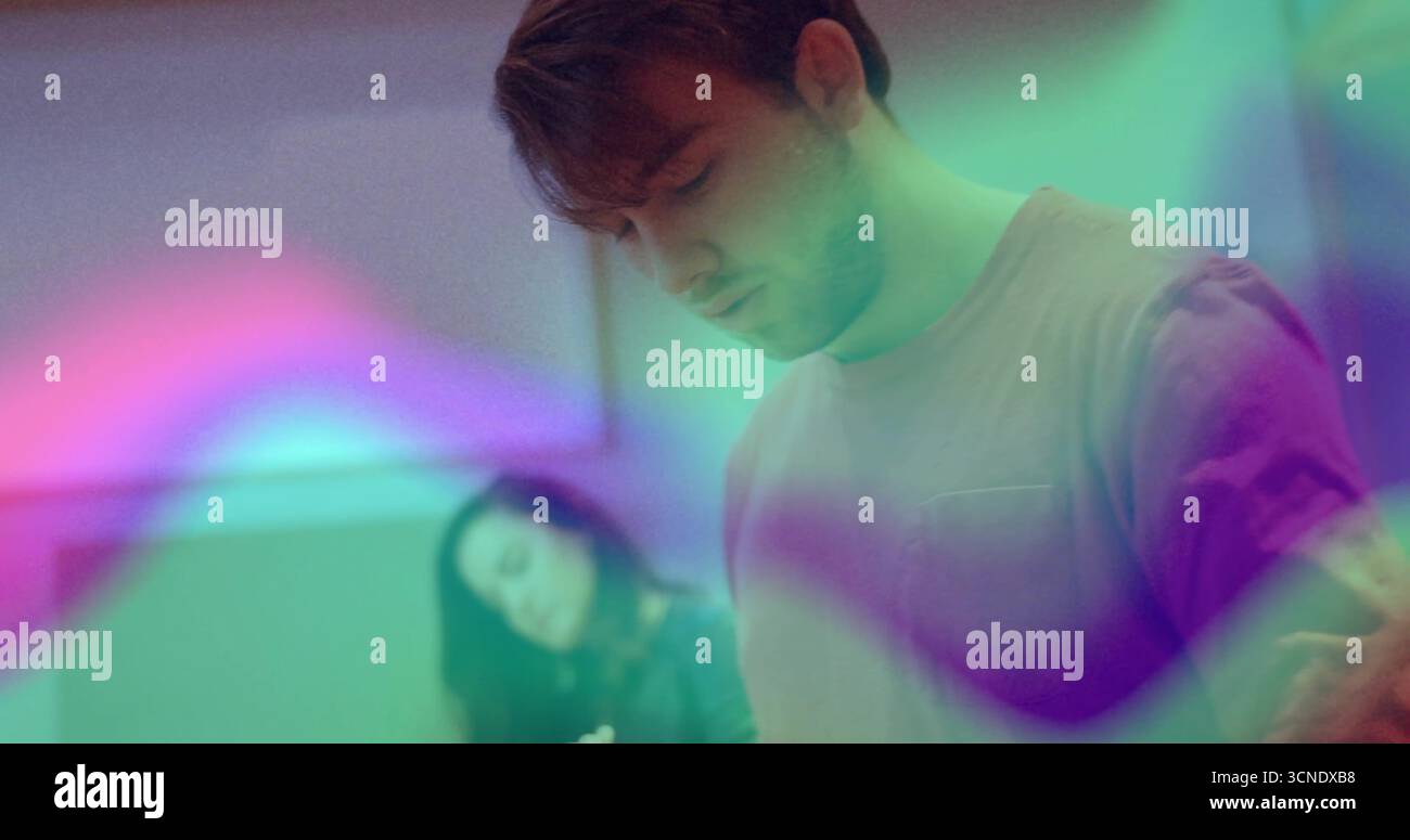 Uomo in piedi concentrato che immerge le proiezioni di luce verde viola rosa in una stanza sparsa, con sfumature ambientali Foto Stock