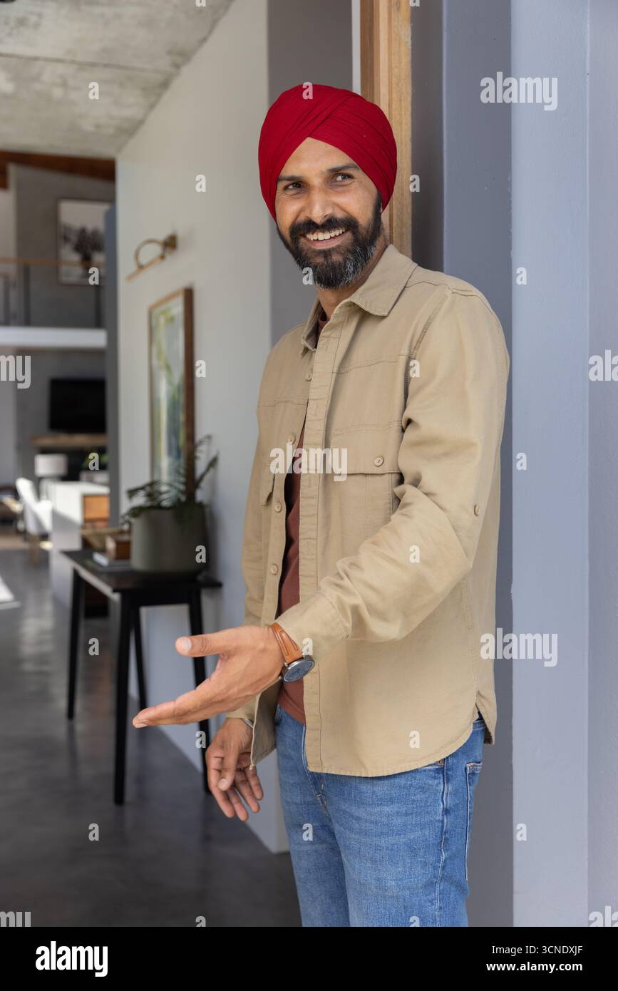 Uomo indiano di mezza età che si estende per mano in un gesto accogliente all'ingresso di casa, pianta in vaso Foto Stock
