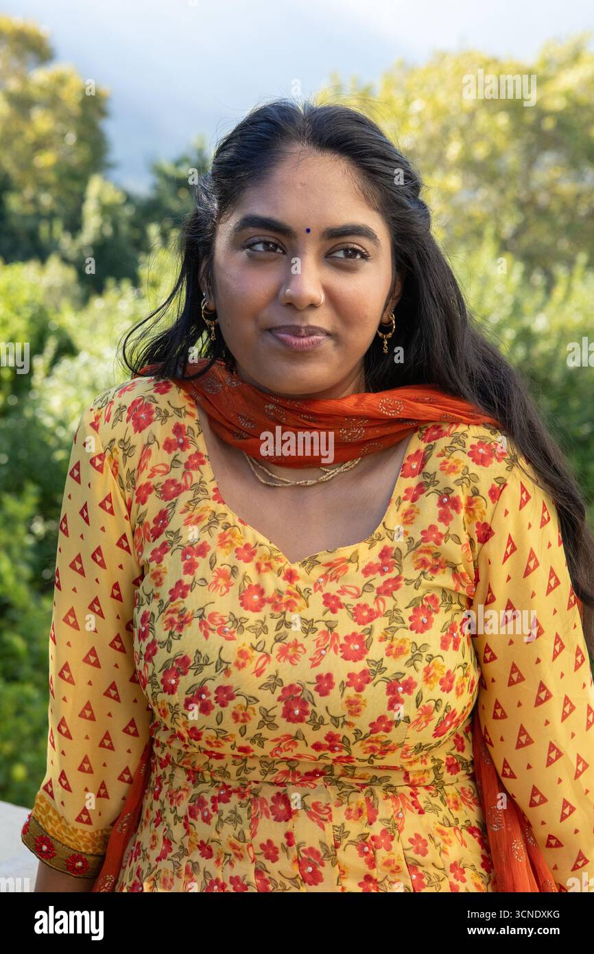 Donna indiana in piedi nel parco che indossa kurta con dupatta arancione e gioielli in oro con bindi Foto Stock