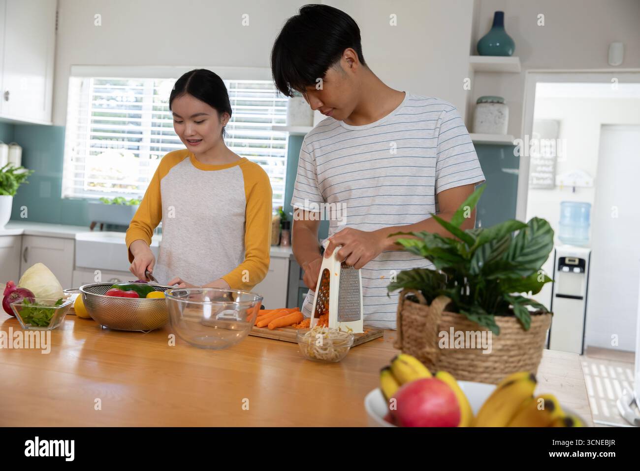 Coppia asiatica che trita peperoni sul tagliere e che grattugia carote sull'isola Kitchen Foto Stock