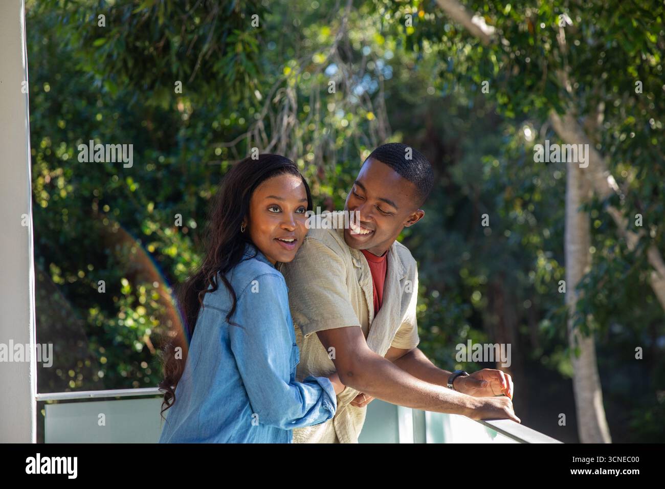 Coppia afroamericana in piedi sul balcone appoggiato su ringhiere di vetro condividendo un'occhiata tenera Foto Stock
