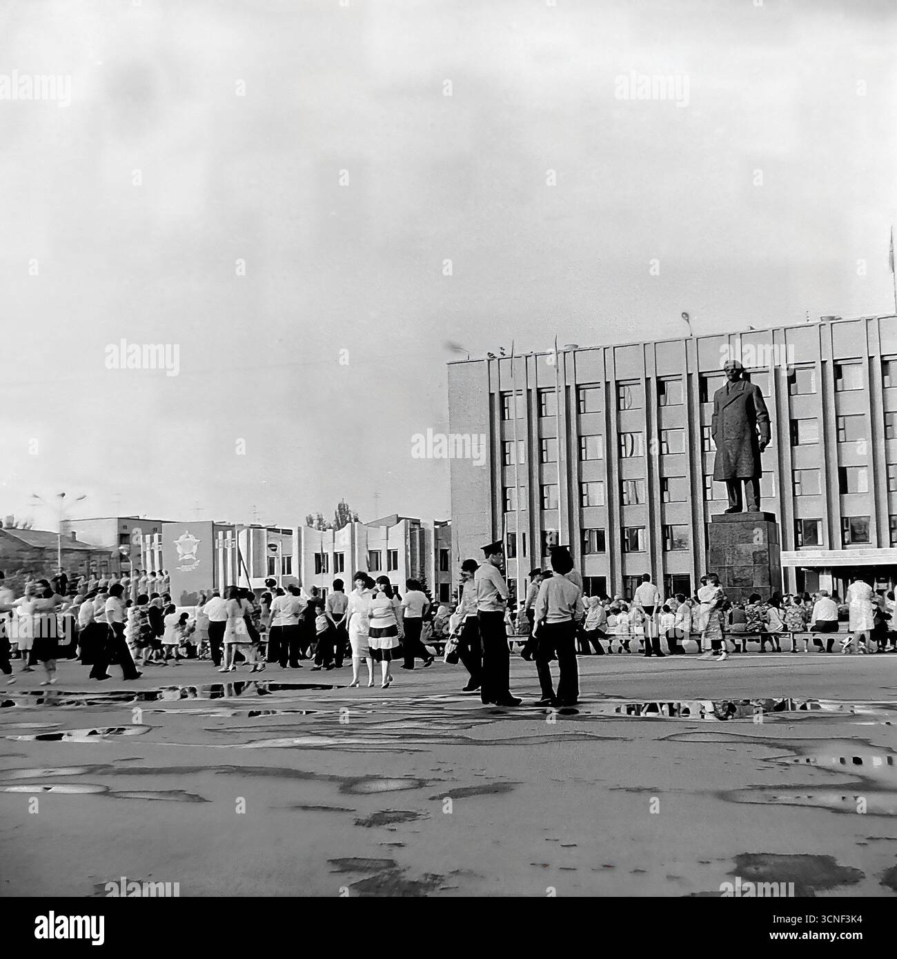 I residenti e le famiglie con bambini passeggiano attraverso la piazza centrale della Rivoluzione d'ottobre (ora piazza Soborna) vicino al monumento Lenin durante la celebrazione della giornata della città a Sloviansk, URSS, il 6 settembre 1985. Questa autentica fotografia di reportage in bianco e nero cattura l'atmosfera vivace di un festival pubblico e di un raduno di massa, con persone che si godono la vacanza insieme nonostante le pozzanghere di una pioggia precedente, mostrando una tipica scena della vita civica dell'epoca sovietica Foto Stock