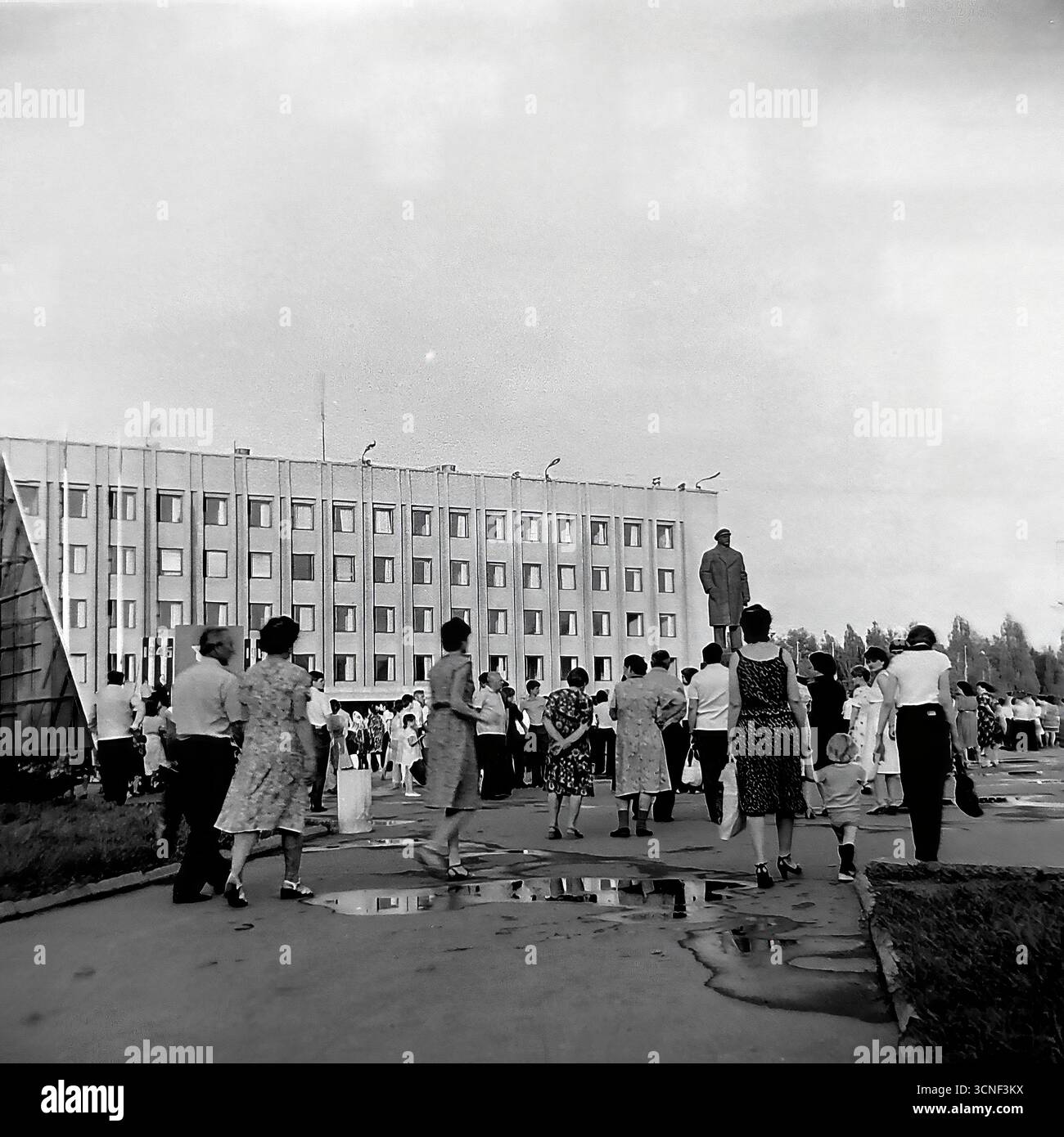 I residenti e le famiglie con bambini passeggiano attraverso la piazza centrale della Rivoluzione d'ottobre (ora piazza Soborna) vicino al monumento Lenin durante la celebrazione della giornata della città a Sloviansk, URSS, il 6 settembre 1985. Questa autentica fotografia di reportage in bianco e nero cattura l'atmosfera vivace di un festival pubblico e di un raduno di massa, con persone che si godono la vacanza insieme nonostante le pozzanghere di una pioggia precedente, mostrando una tipica scena della vita civica dell'epoca sovietica Foto Stock