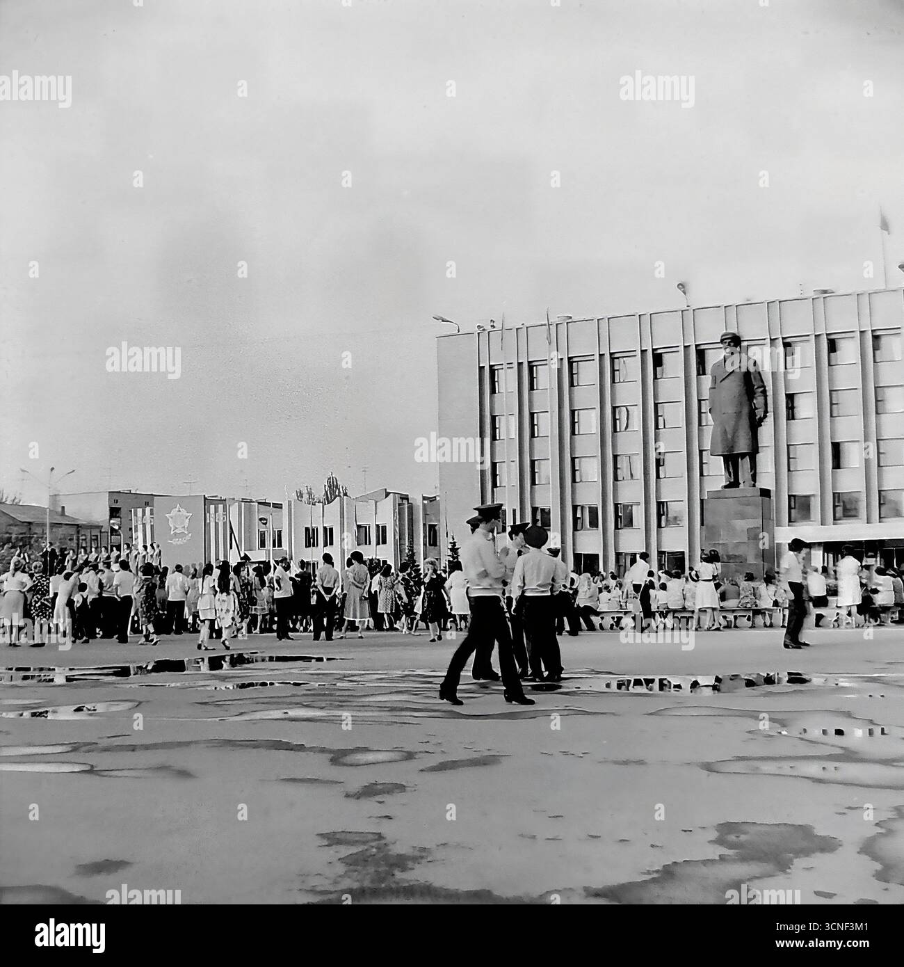 I residenti e le famiglie con bambini passeggiano attraverso la piazza centrale della Rivoluzione d'ottobre (ora piazza Soborna) vicino al monumento Lenin durante la celebrazione della giornata della città a Sloviansk, URSS, il 6 settembre 1985. Questa autentica fotografia di reportage in bianco e nero cattura l'atmosfera vivace di un festival pubblico e di un raduno di massa, con persone che si godono la vacanza insieme nonostante le pozzanghere di una pioggia precedente, mostrando una tipica scena della vita civica dell'epoca sovietica Foto Stock