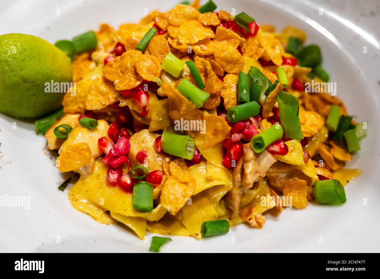 piatto di curry di pollo con pasta melograno, lime guarnito con fiocchi di mais e erba cipollina Foto Stock