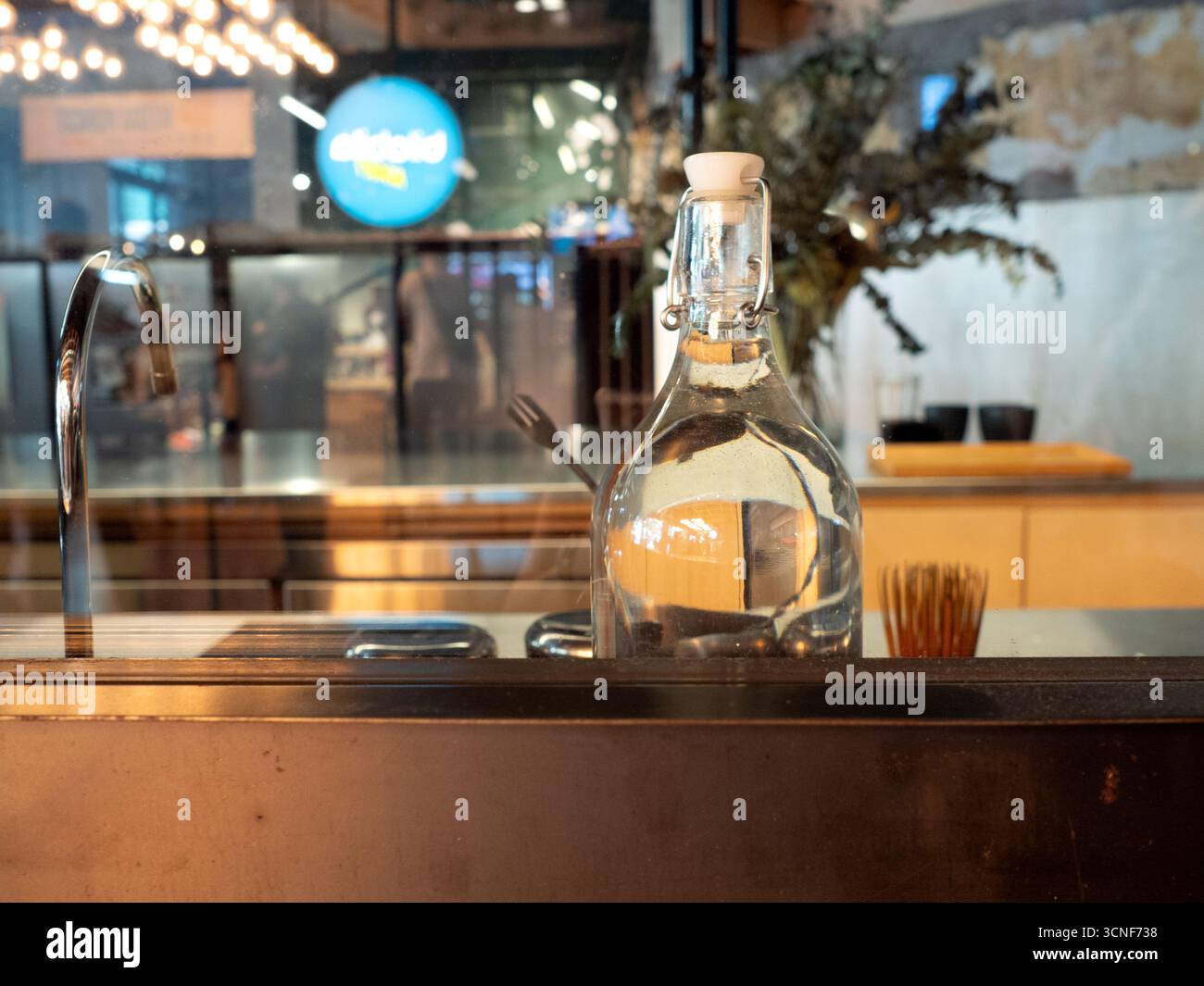 Caraffa d'acqua di vetro con coperchio a altalena sul bancone del bar o del ristorante, design semplice che riflette il servizio informale di ristorazione e bevande. Foto Stock