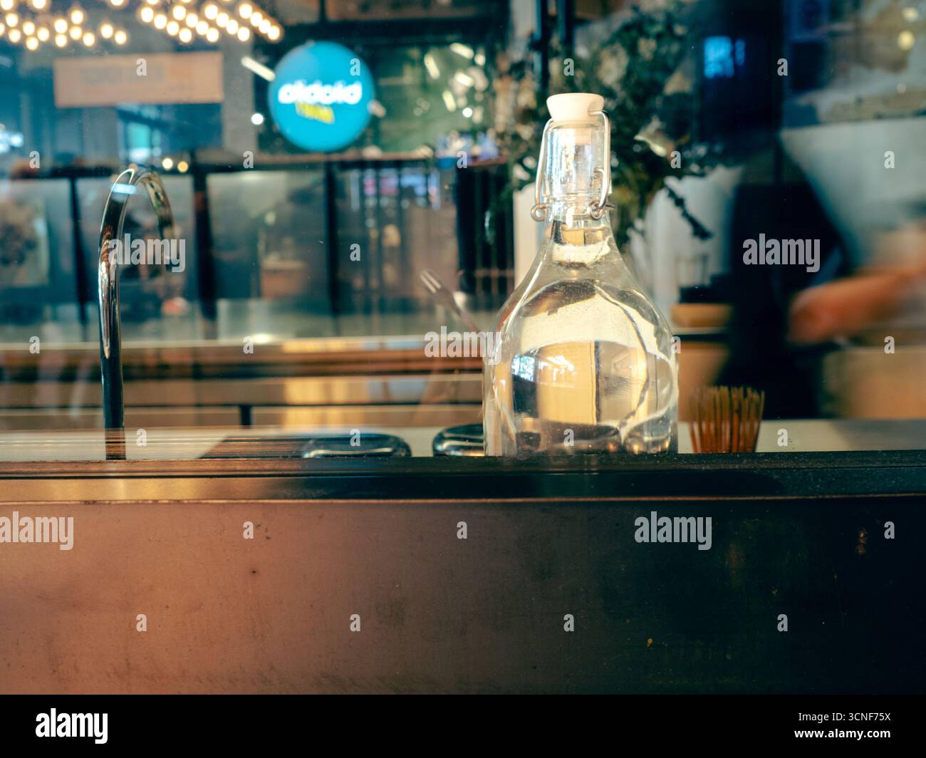 Caraffa d'acqua di vetro con coperchio a altalena sul bancone del bar o del ristorante, design semplice che riflette il servizio informale di ristorazione e bevande. Foto Stock