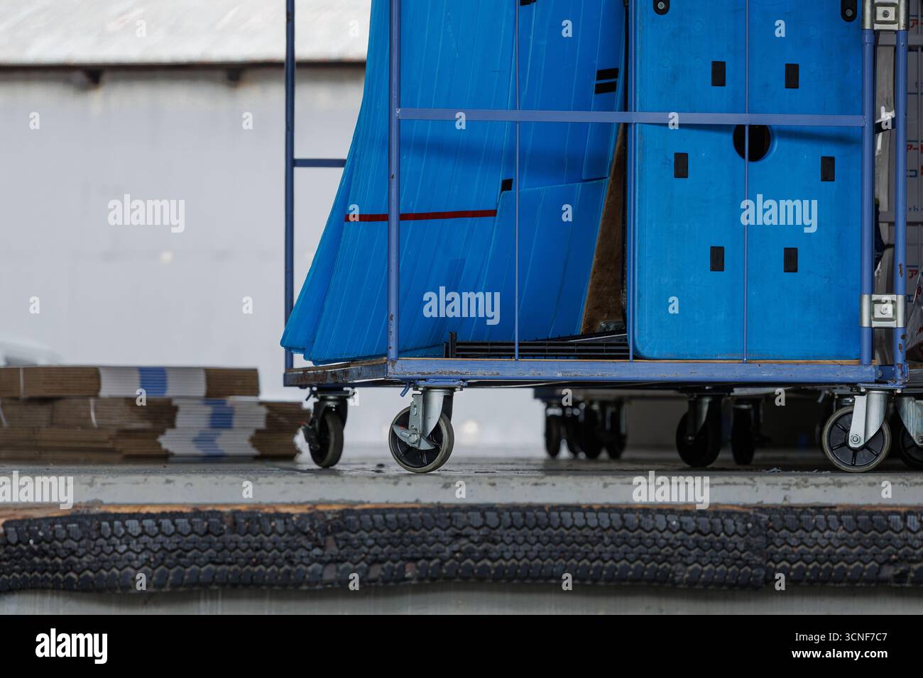 Banchina di carico del centro di distribuzione con carrello a ruote blu impilato con pannelli blu e fasci di cartone inutilizzati su una superficie in cemento. Foto Stock