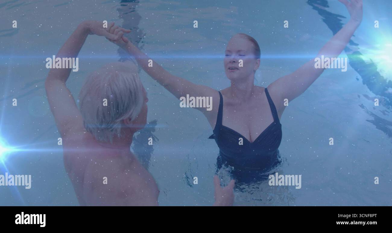 Alzare le braccia coppia senior tenendo le mani in piscina, indossando costume da bagno scuro e costume da bagno Foto Stock