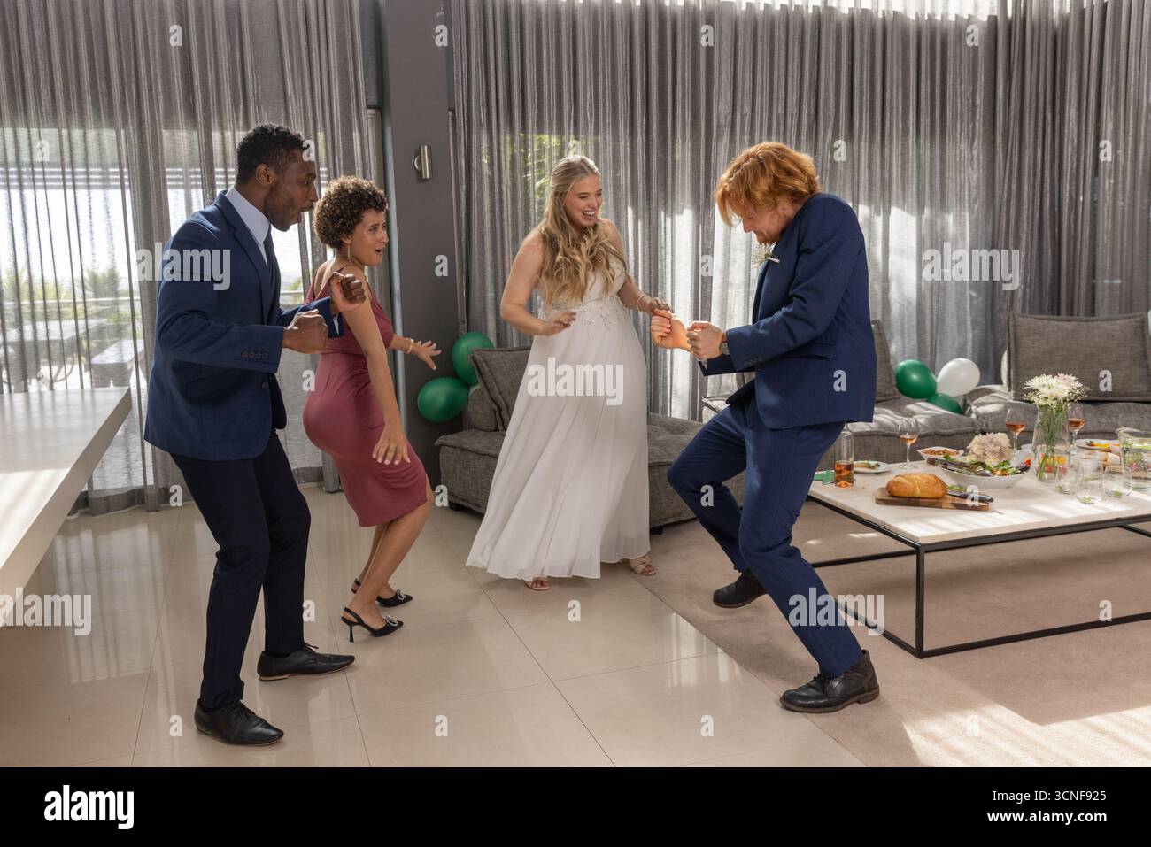 Diversi ospiti di nozze che ballano con sposi e sposi nell'area soggiorno vicino a tavolino da caffè e palloncini Foto Stock