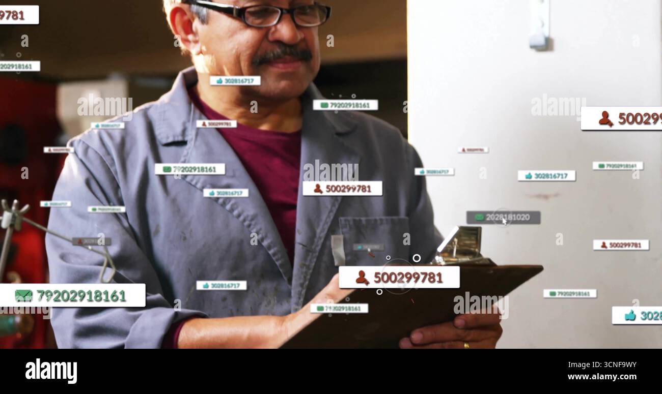 Esame degli appunti, tecnico che indossa una giacca grigia e una camicia rossa in officina con etichette digitali Foto Stock