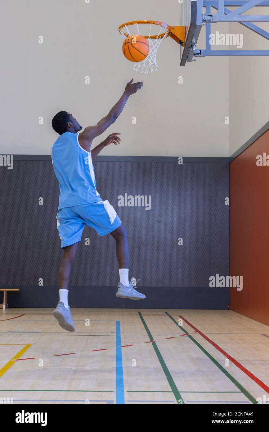 Giocatore di basket maschile che si esibisce a strati verso il cerchio all'interno della palestra sul campo con linee Foto Stock