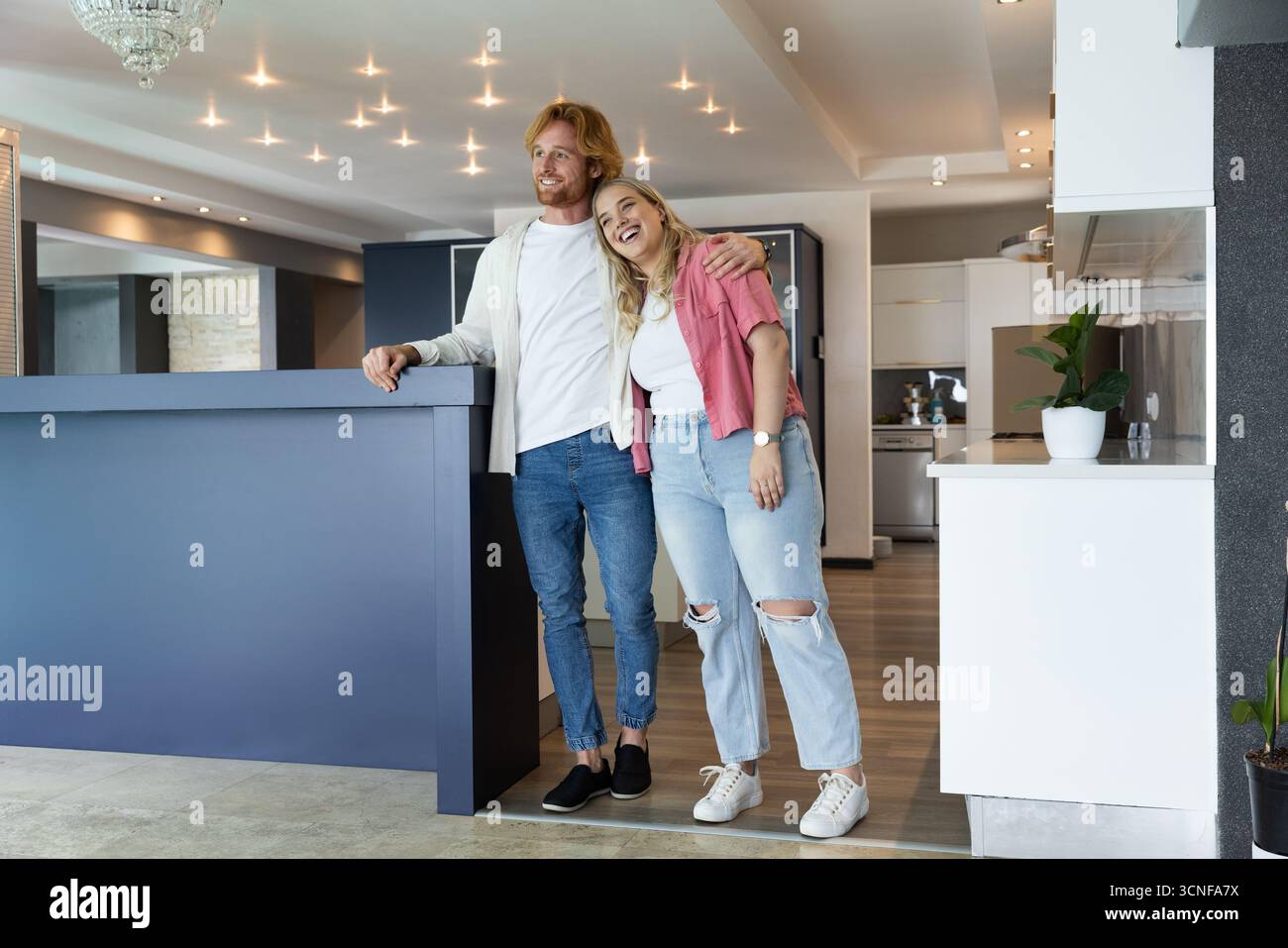 Coppia sorridente e appoggiata dietro l'isola della cucina blu navy nella cucina a vista Foto Stock