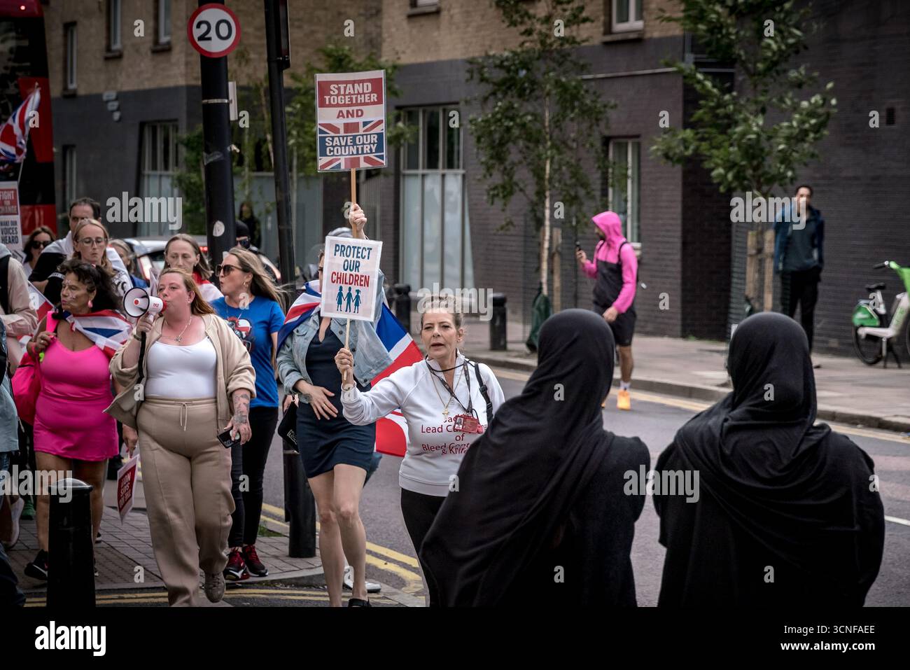Londra, Regno Unito. 20 settembre 2025. Una donna musulmana locale guarda i manifestanti anti anti-migranti marciare attraverso l'Isola dei cani con bandiere e cartelli come parte delle continue dimostrazioni contro il Britannia International Hotel a Canary Wharf che ospita richiedenti asilo. Crediti: Guy Corbishley/Alamy Live News Foto Stock