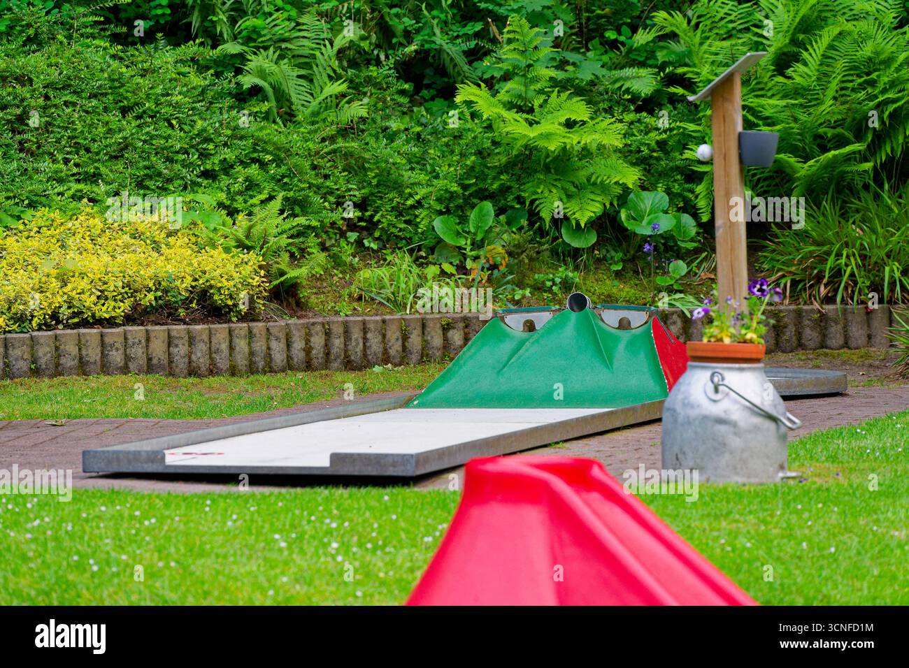 Una corsia di putting curvilinea si snoda attraverso il prato, caratterizzato da una gobba verde e una rampa rossa brillante. Ambiente ricreativo per famiglie adatto a brochure, p Foto Stock