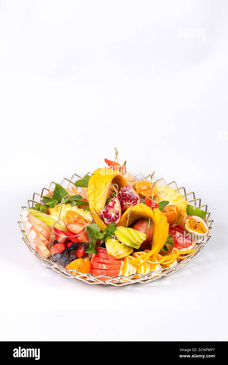 Piatto di frutta vivace con ananas, mango, pompelmo e menta. Presentazione elegante su uno sfondo bianco pulito. Foto Stock