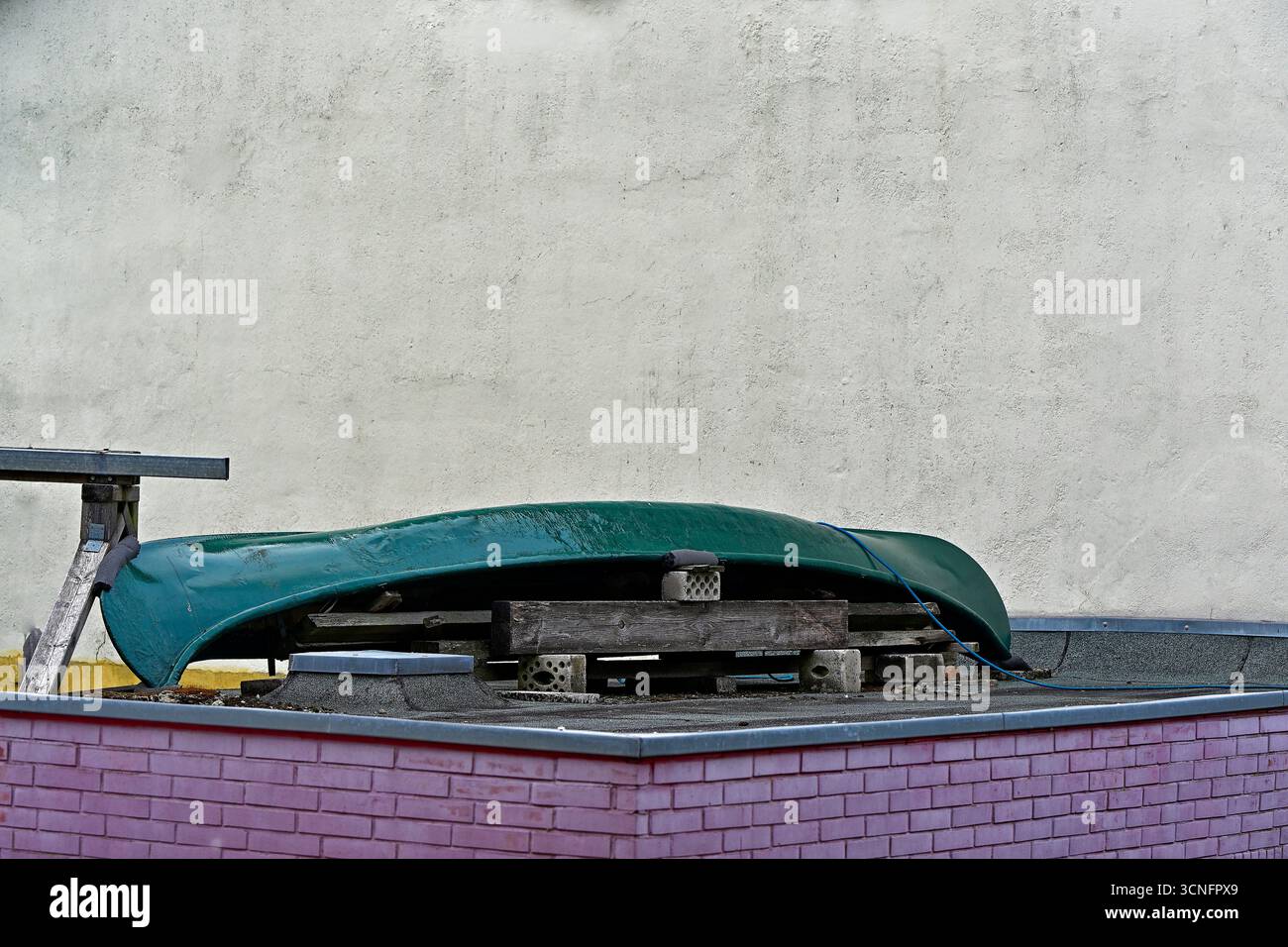 edificio annesso in mattoni dipinti di rosa con pallet sul tetto che supporta un kayak verde scuro. Spazio di archiviazione casual per marchi di viaggi, annunci di articoli per esterni, articoli per la casa Foto Stock