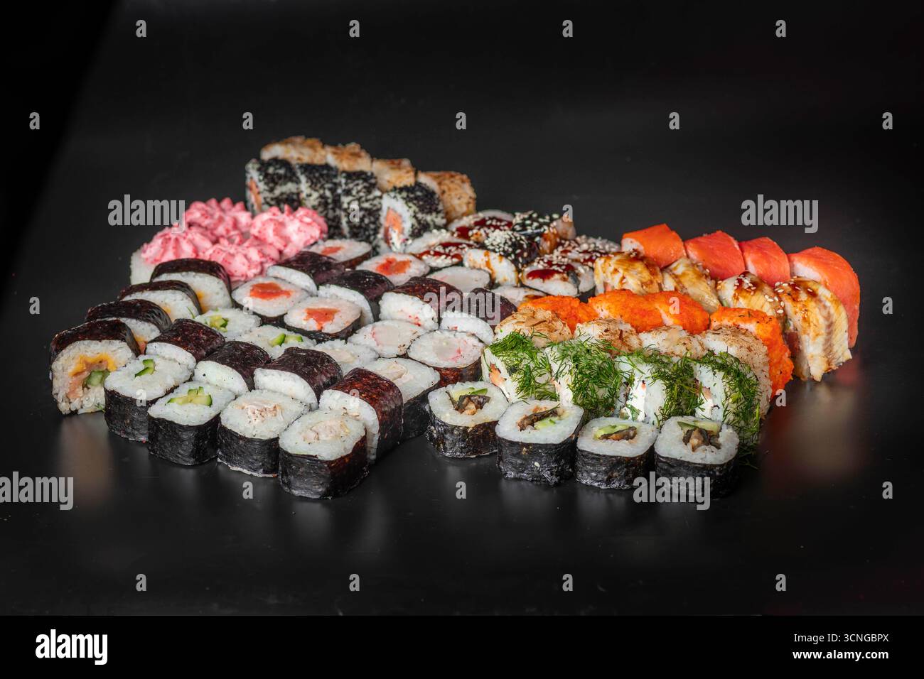 Una varietà di sushi roll disposti su una superficie nera. Comprende maki, nigiri e panini speciali con guarnizioni colorate e decorazioni. Foto Stock