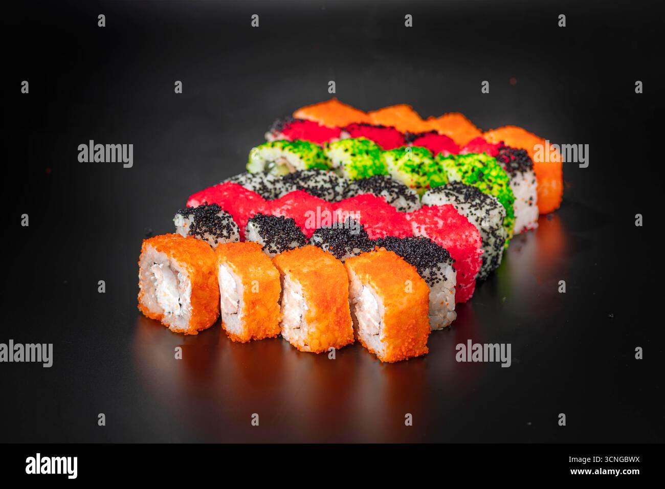 Un variopinto assortimento di sushi roll disposti ordinatamente su una superficie nera. I rotoli sono caratterizzati da vari condimenti e ripieni, mostrando colori vivaci e Foto Stock