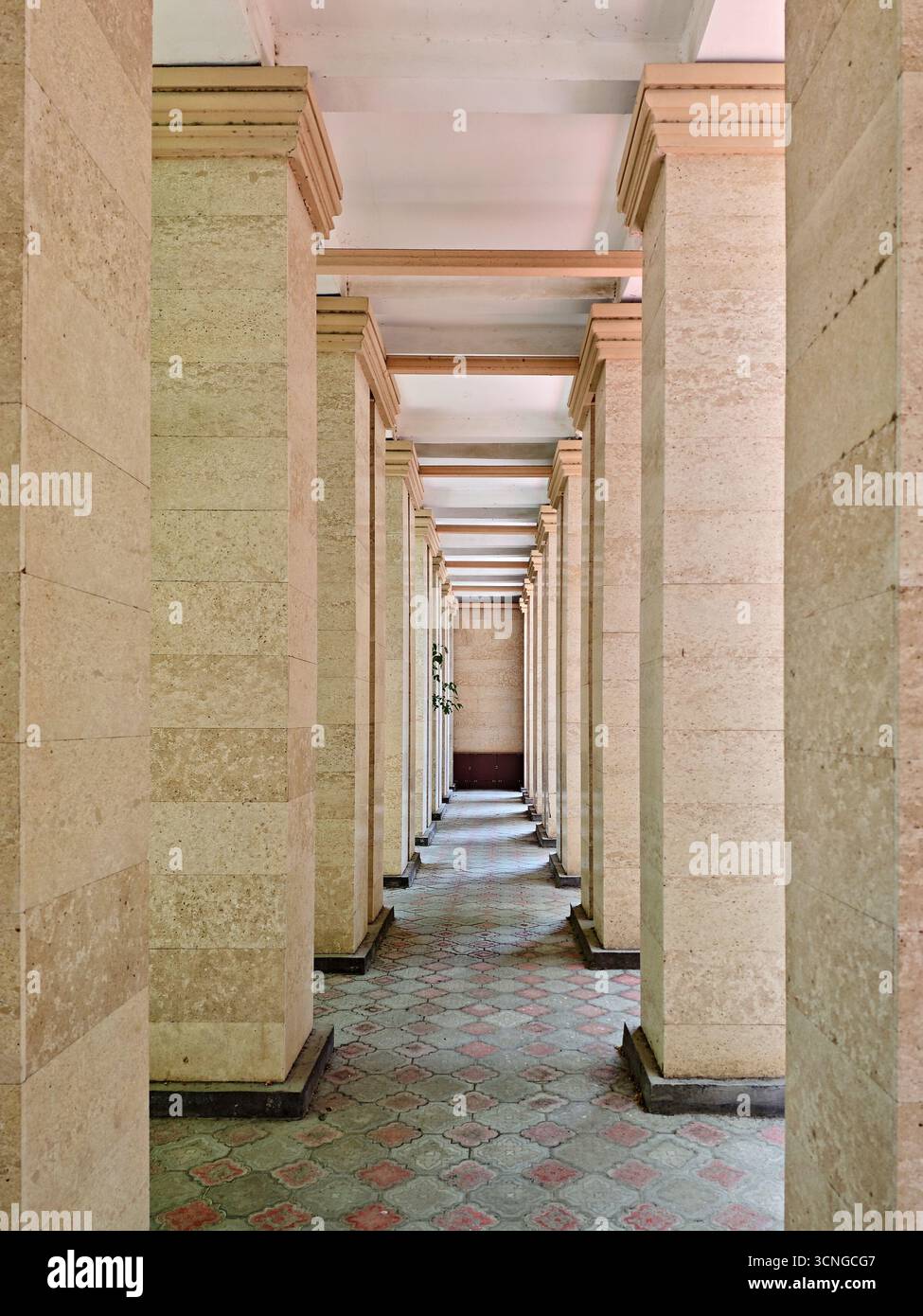 Vista simmetrica di un lungo corridoio coperto (arcade), formato da file di colonne beige chiare all'interno dell'edificio del Centro regionale di cardiologia Atyrau. Foto Stock