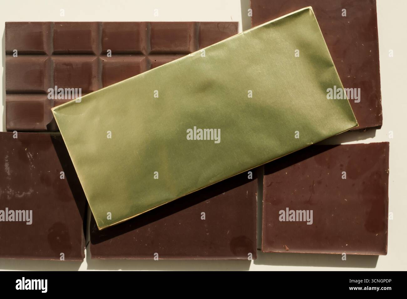 Tavoletta di cioccolato in carta laminata gialla su sfondo con barrette di cioccolato srotolate. Copia spazio. Foto Stock